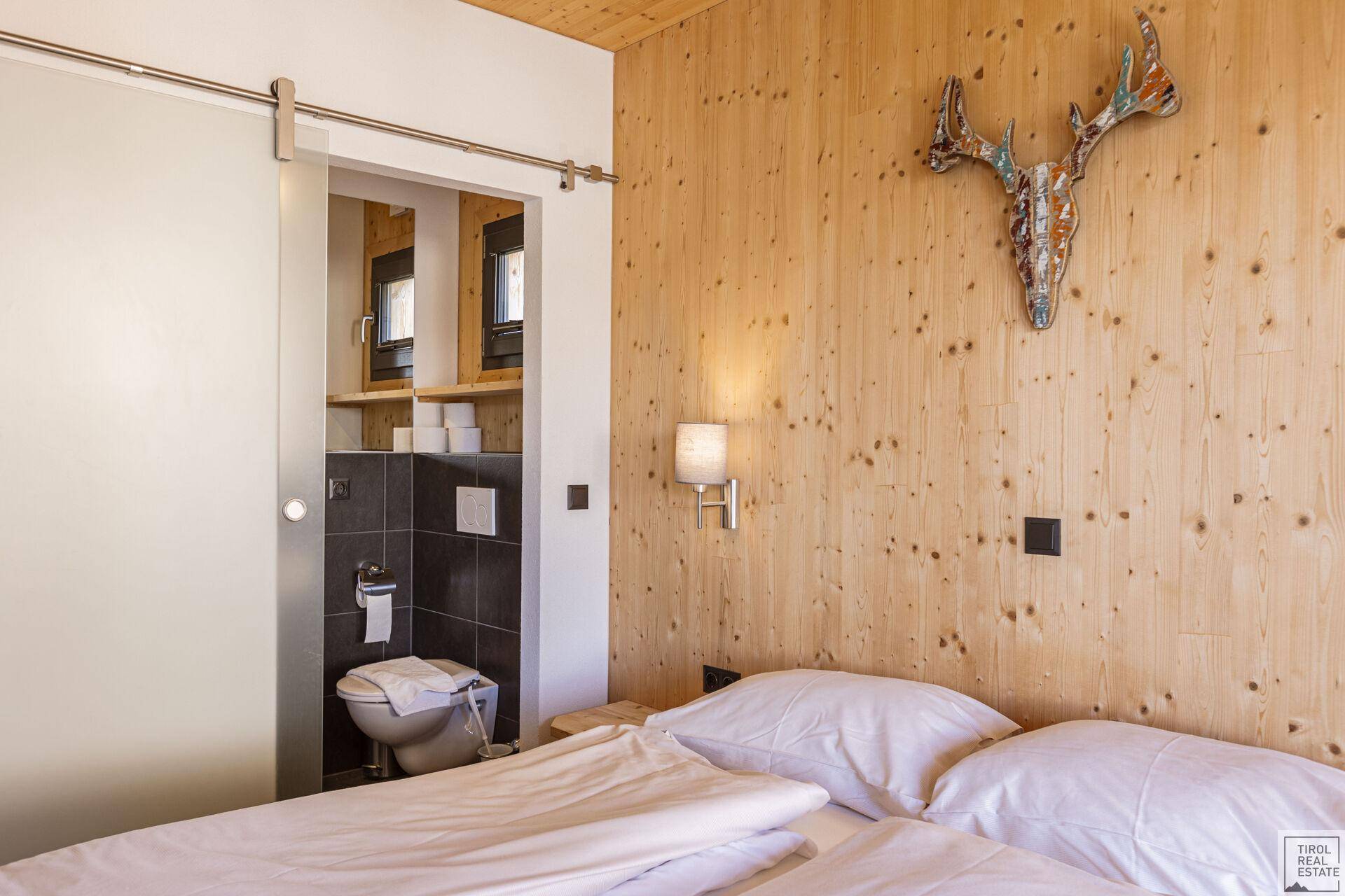 Schlafzimmer mit Holzwänden, Hirschgeweih-Dekor und Zugang zu einem WC.