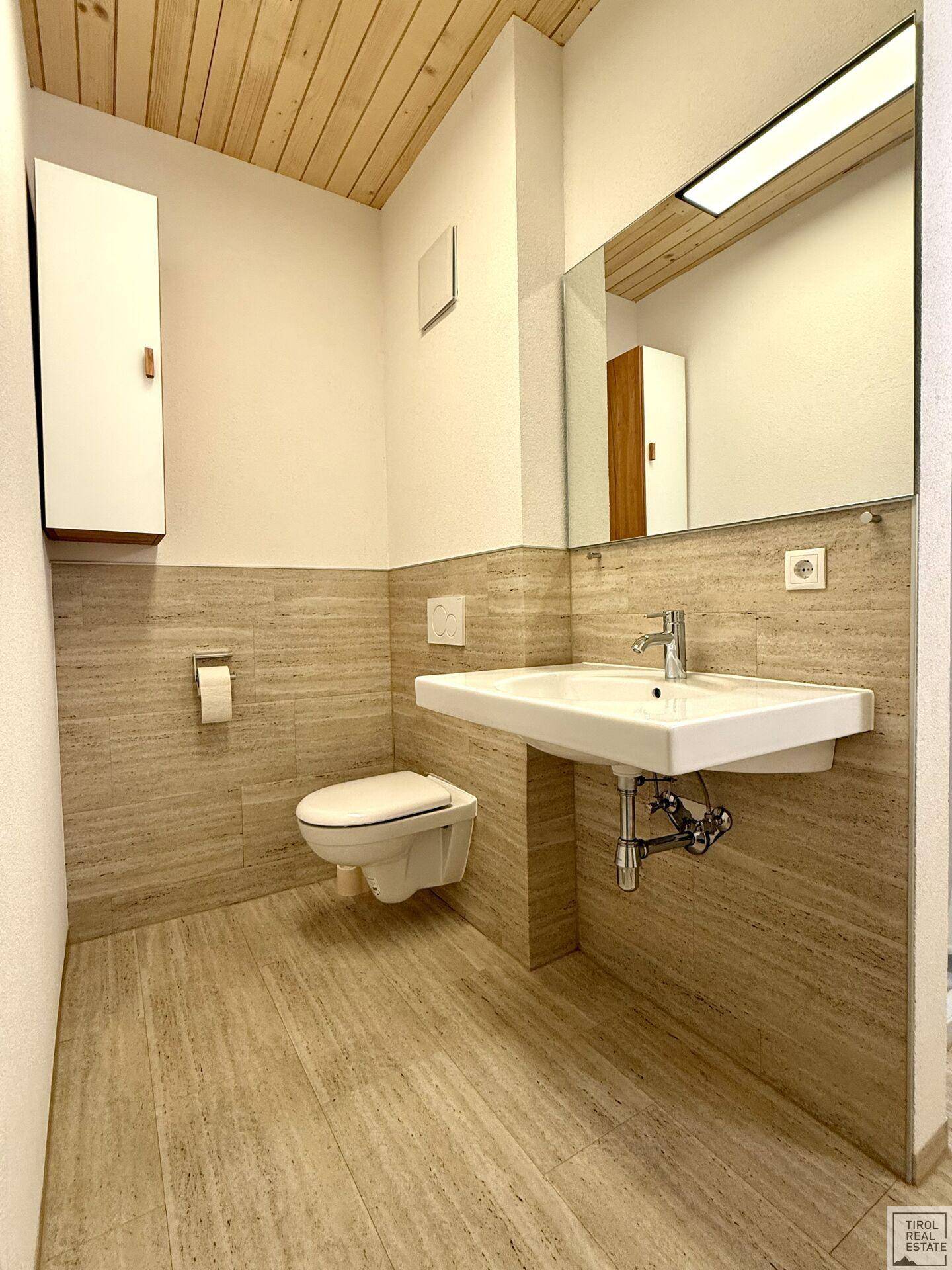Modernes Badezimmer mit Holzdachschräge, beigefarbenen Fliesen und wandhängender Toilette.