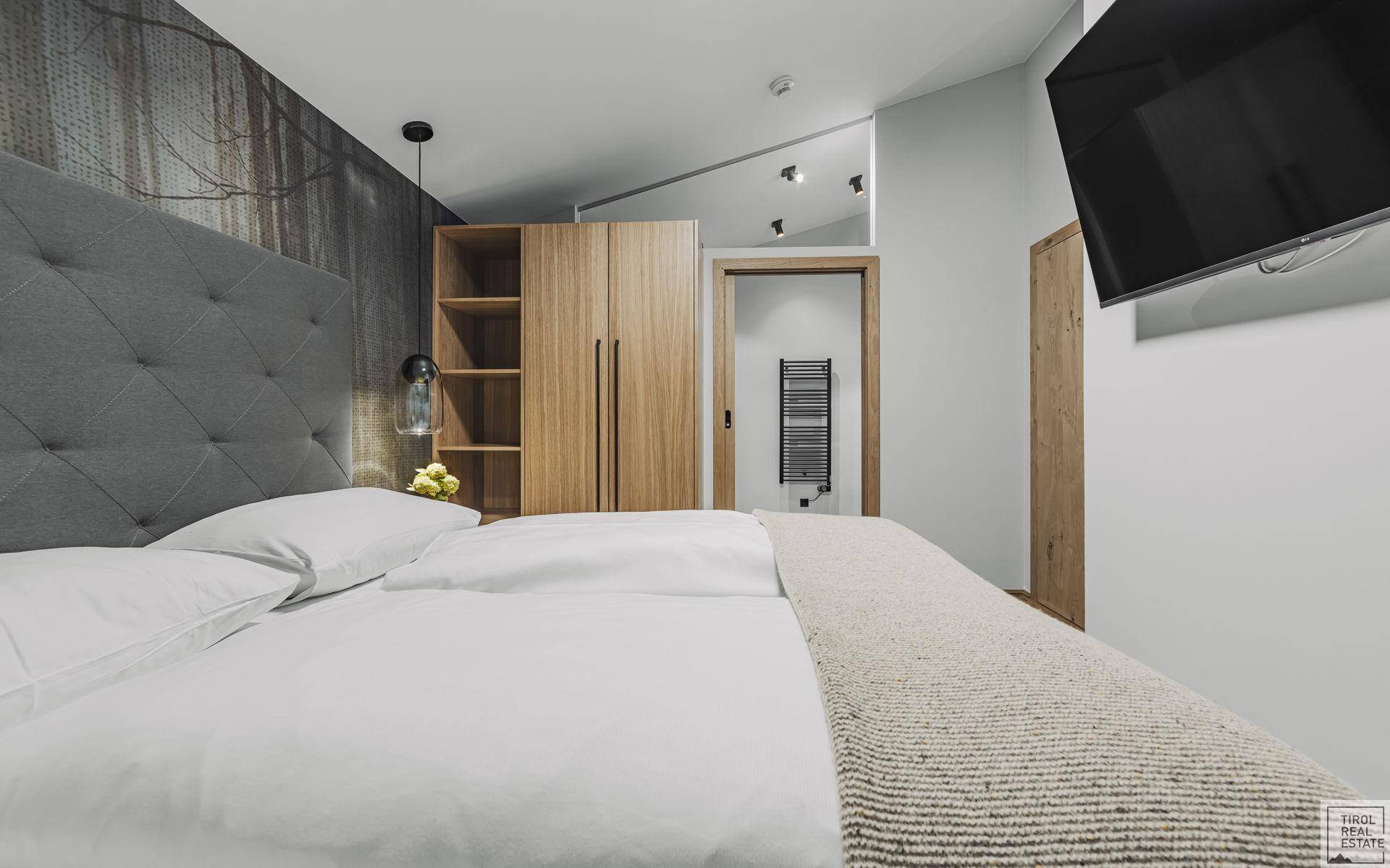 Modernes Schlafzimmer mit großem Bett, Holzkleiderschrank und Zugang zu einem angrenzenden Badezimmer.