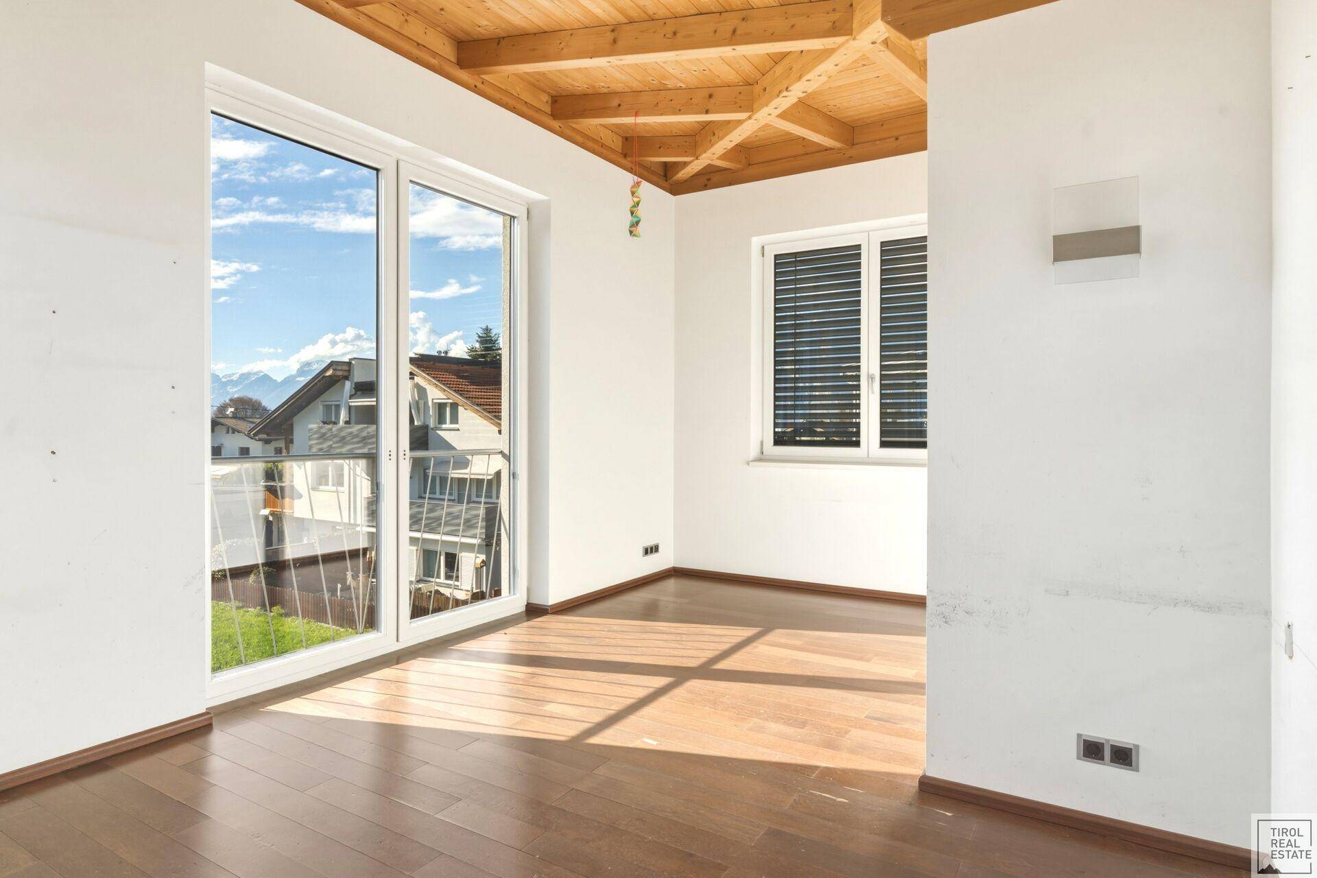 Schlafzimmer mit Holzboden, Holzbalkendecke und großen Fenstern mit Bergblick.