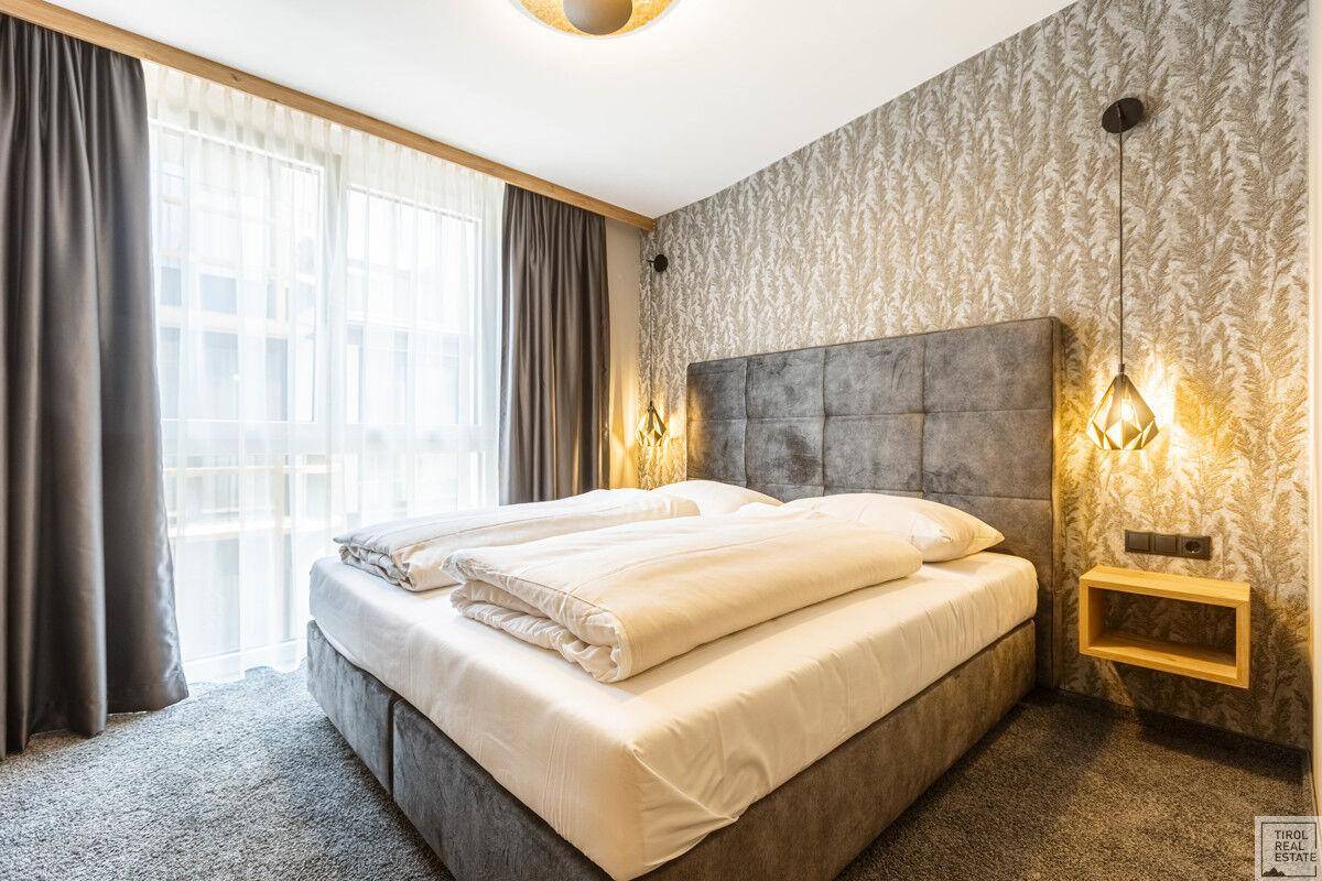 Helles Schlafzimmer mit großem Doppelbett, Nachttischen und Fenster mit Bergblick.