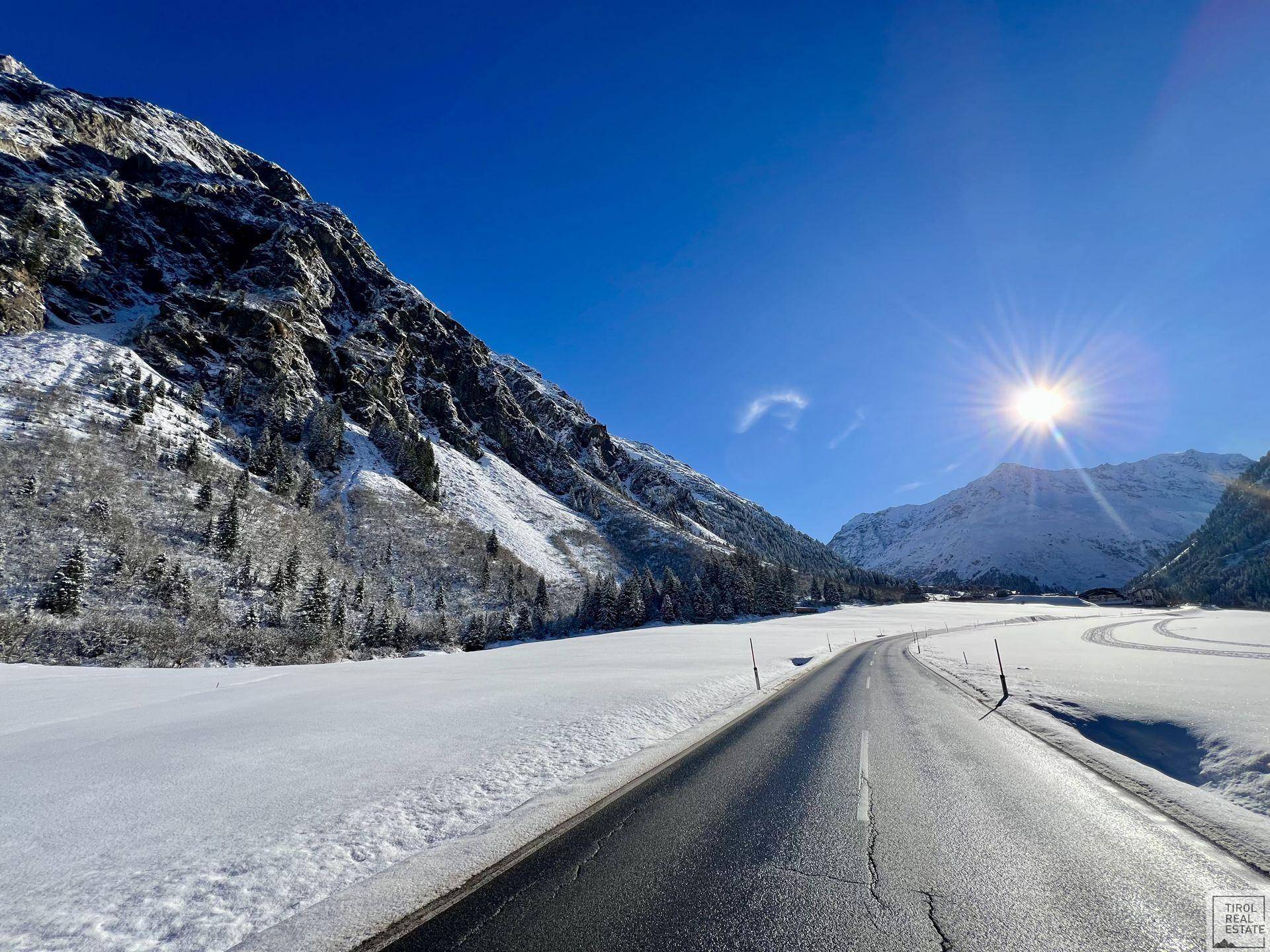 Sonnige Winterlandschaft mit verschneiten Bergen und einer Straße, die durch das Tal führt.