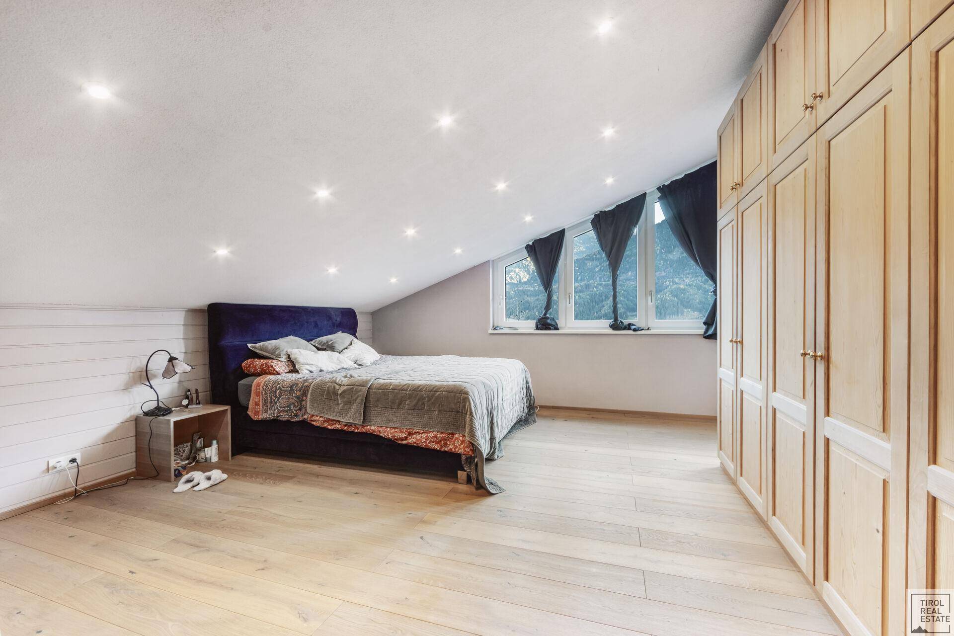 Helles Schlafzimmer im Dachgeschoss mit Holzboden und Einbauschränken.