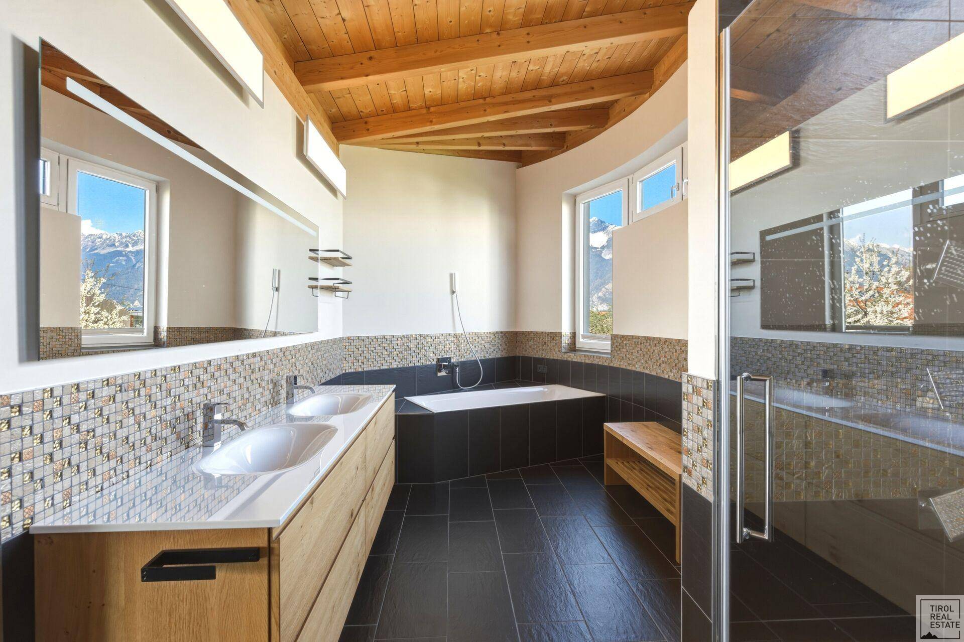Modernes Badezimmer mit Doppelwaschbecken, Badewanne und großer Dusche, umgeben von Mosaikfliesen.