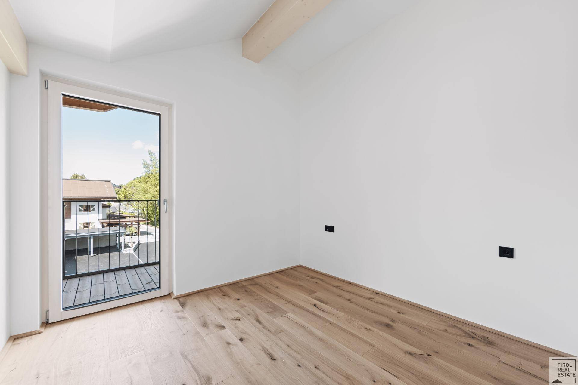 Helles Schlafzimmer mit Parkettboden und Zugang zu einem französischen Balkon.