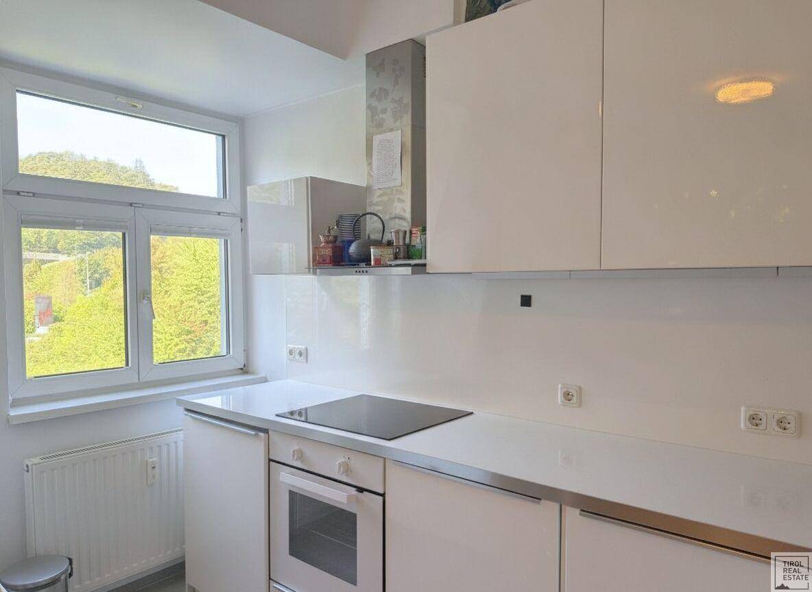 Helle, moderne Küche mit weißen Schränken, Induktionskochfeld und Fenster mit Blick ins Grüne.