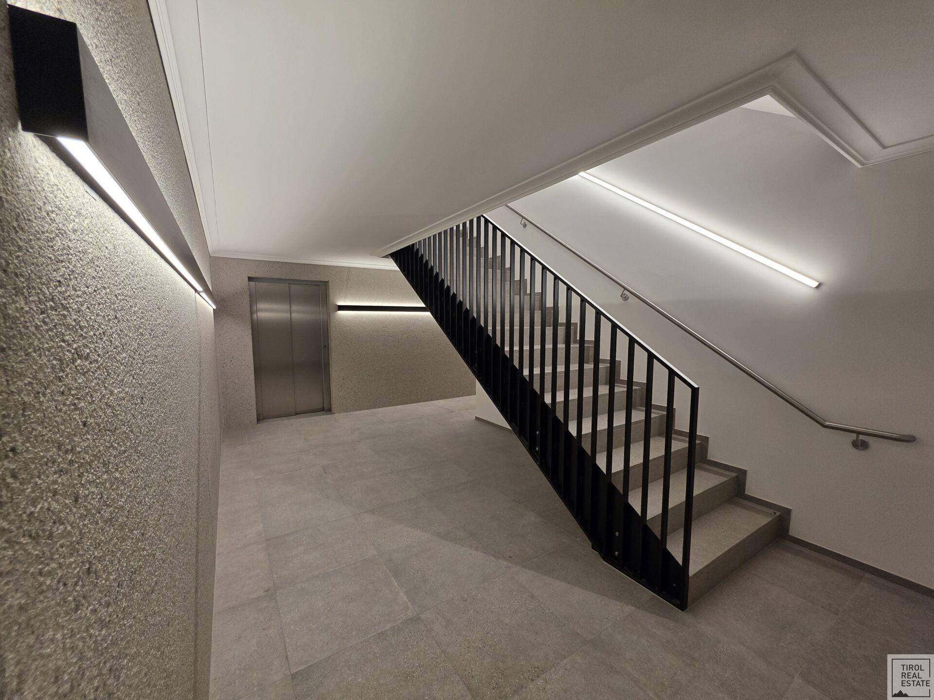 Helles Treppenhaus mit modernem Aufzug und minimalistischer Beleuchtung in einem Neubau.