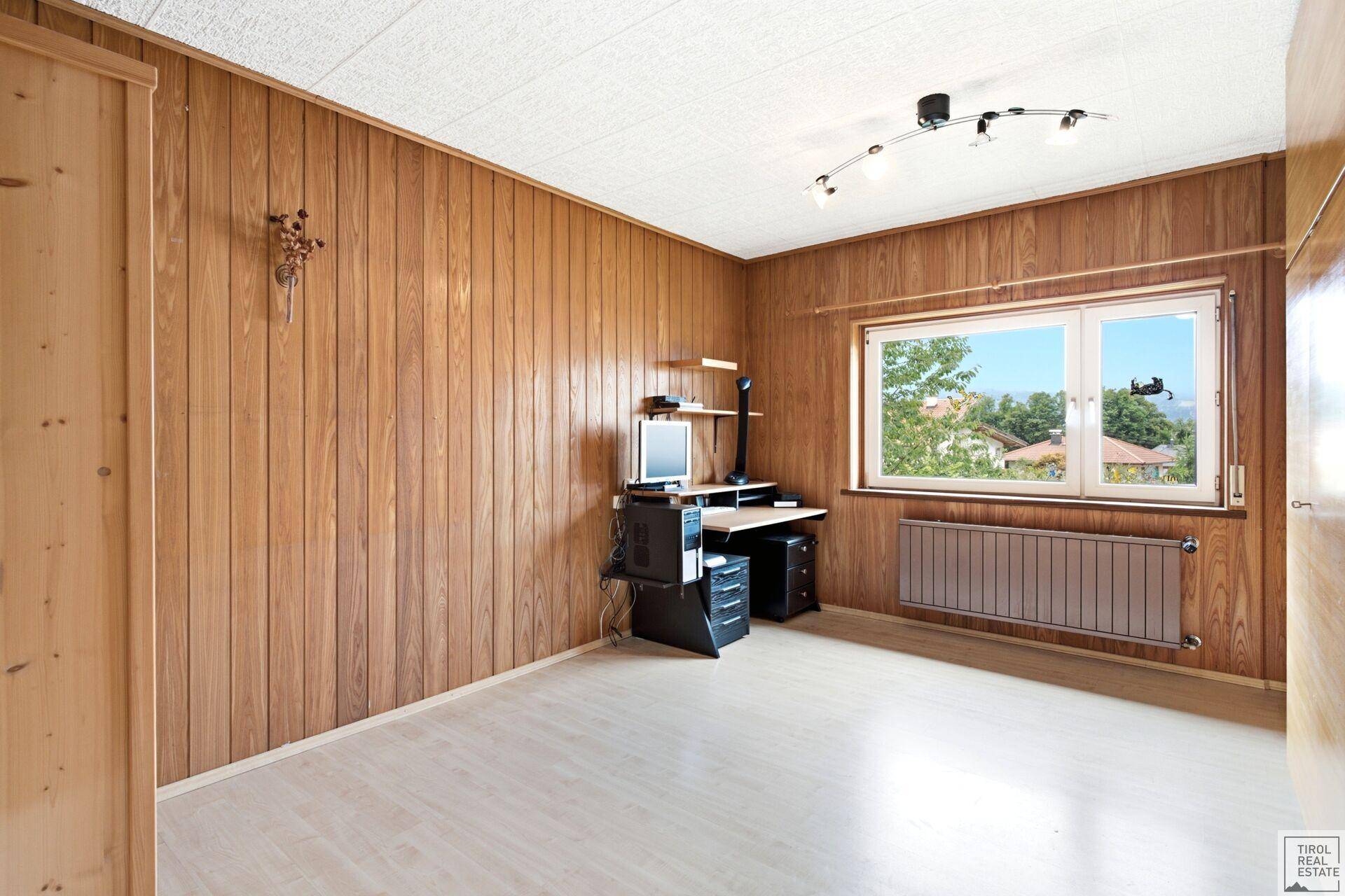 Helles Arbeitszimmer mit Holzvertäfelung, Laminatboden und Blick ins Grüne.