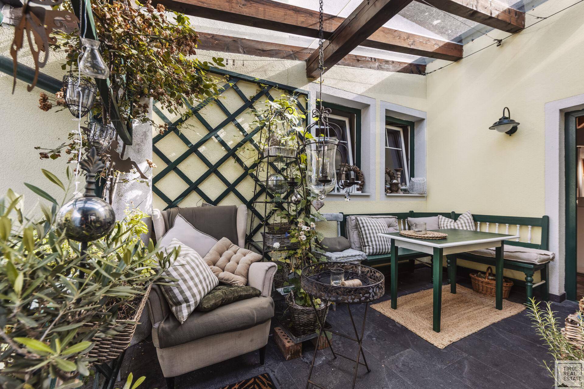 Überdachte Terrasse mit gemütlicher Sitzecke, vielen Pflanzen und Blick ins Grüne.