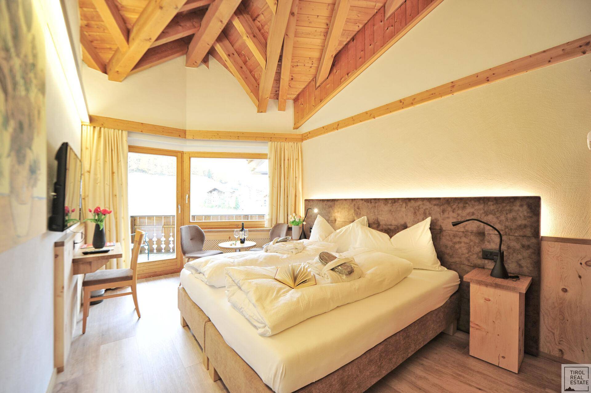 Geräumiges Schlafzimmer mit Holzbalken, großem Bett und Zugang zu einem Balkon mit Aussicht.