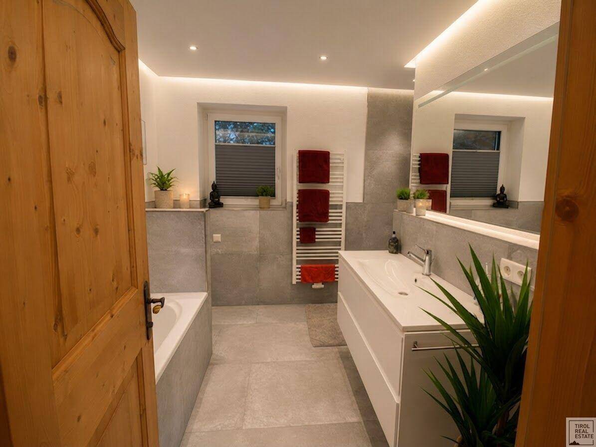 Modernes Badezimmer mit Badewanne, großem Waschtisch, grauen Fliesen und einem beheizten Handtuchhalter.