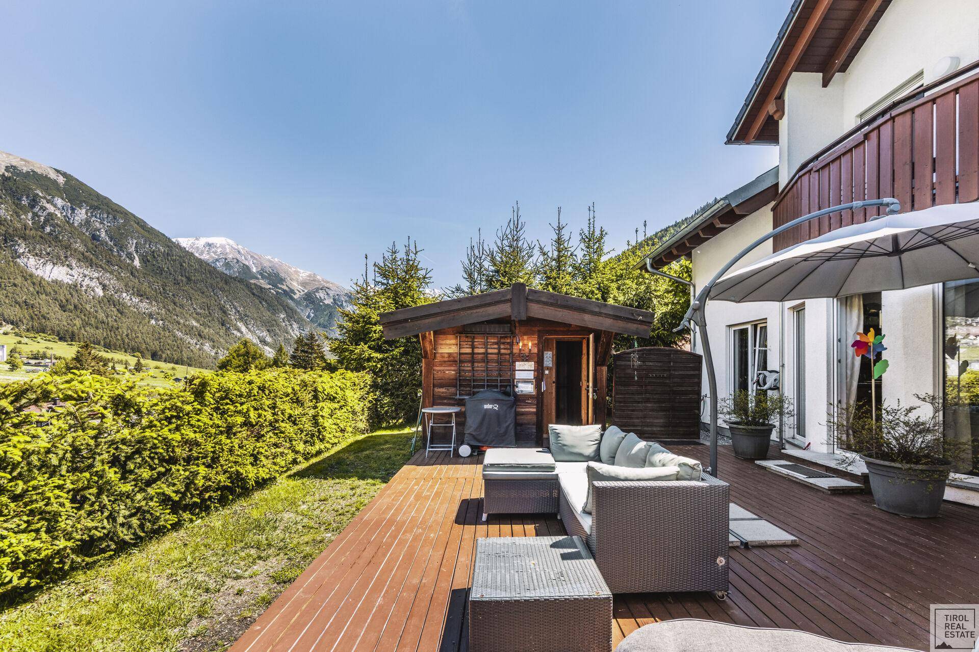 Holzterrasse mit Lounge-Möbeln und Hecke, die Privatsphäre und Bergblick bietet.
