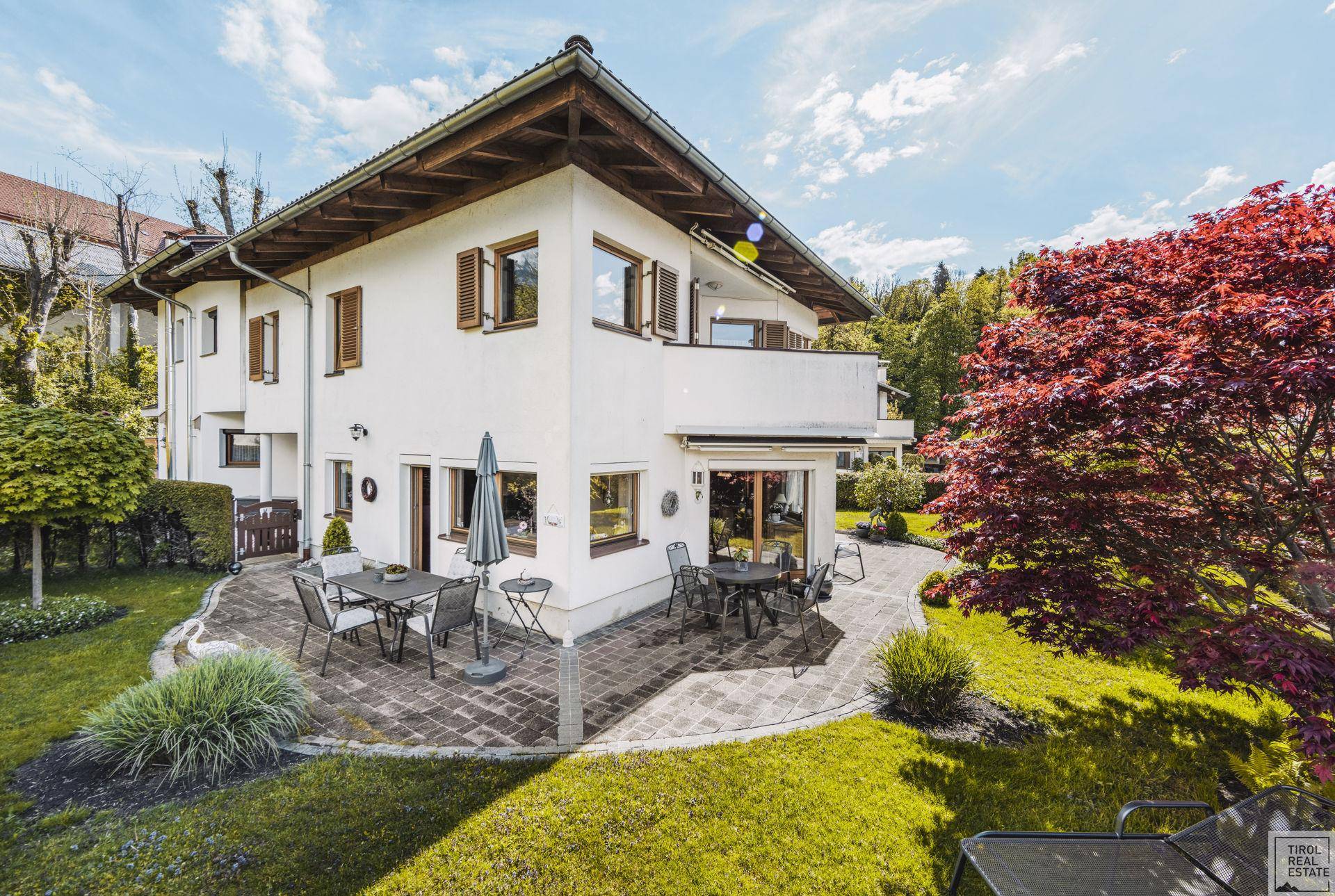 Geräumige Terrasse mit Esstisch und Stühlen, umgeben von einem gepflegten Garten und Bergblick.