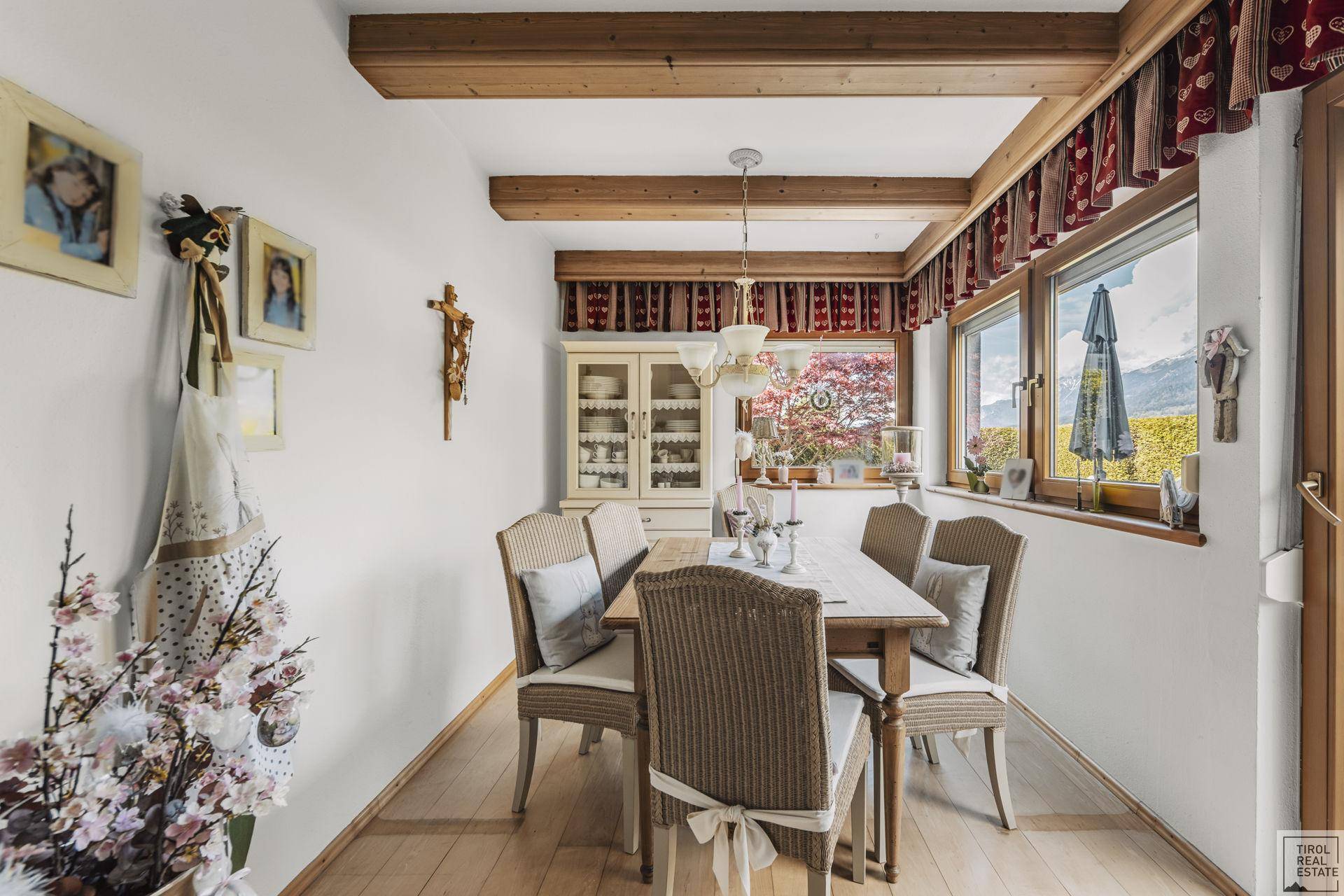 Esszimmer mit Holztisch, Stühlen und Blick auf die Berge und den Garten durch große Fenster.