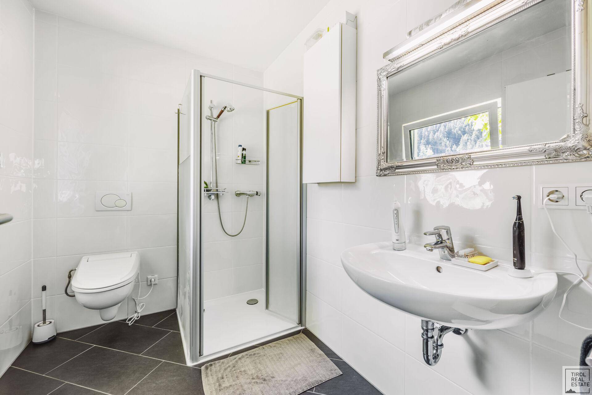 Modernes Badezimmer mit Dusche, wandhängendem WC und großem Spiegel.
