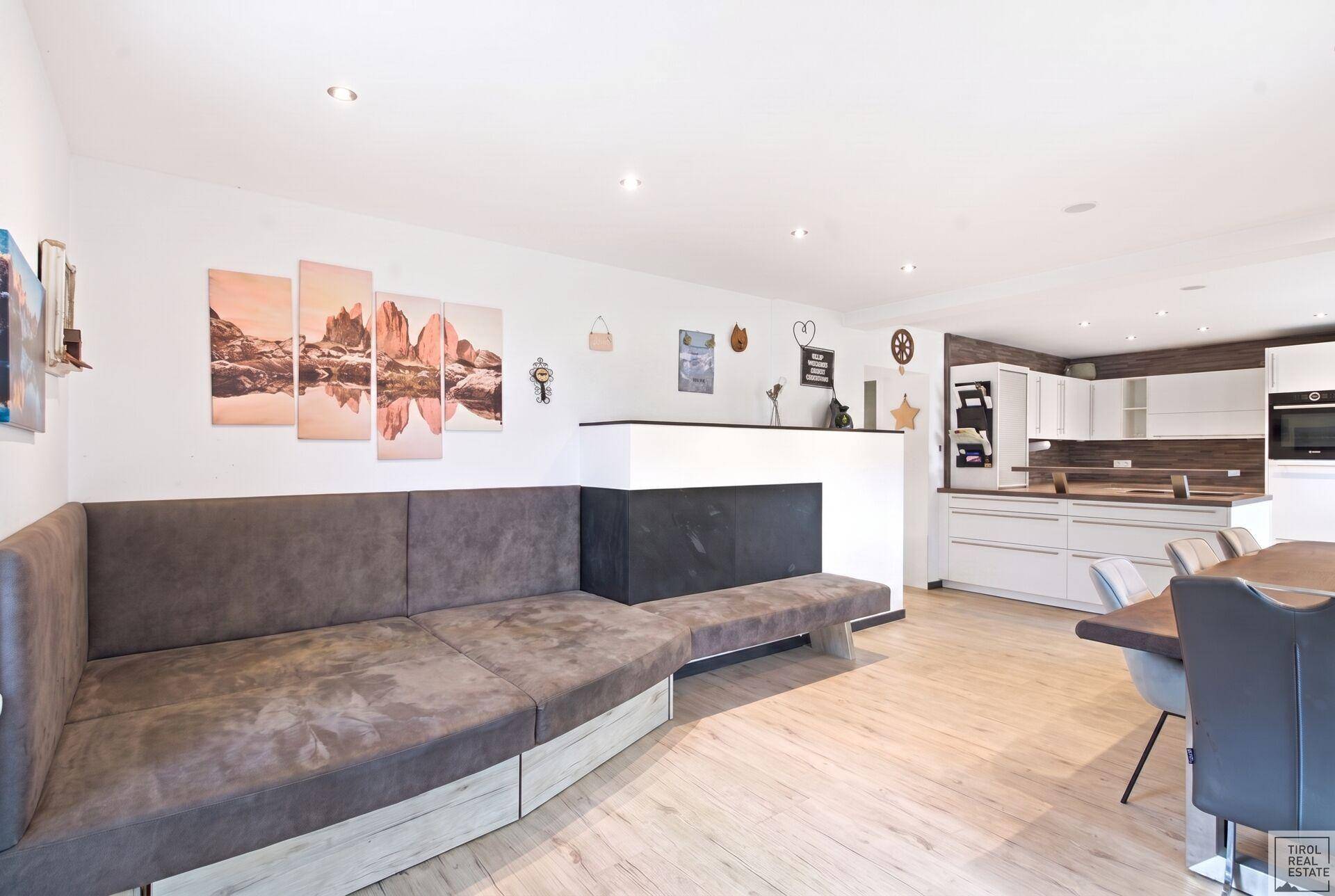 Gemütlicher Wohnbereich mit großem Sofa und Blick auf die offene Küche mit Holzboden.