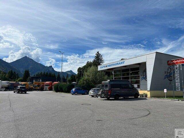 Außenansicht des Cafés und Restaurants mit Parkplatz und beeindruckendem Bergblick unter blauem Himmel.