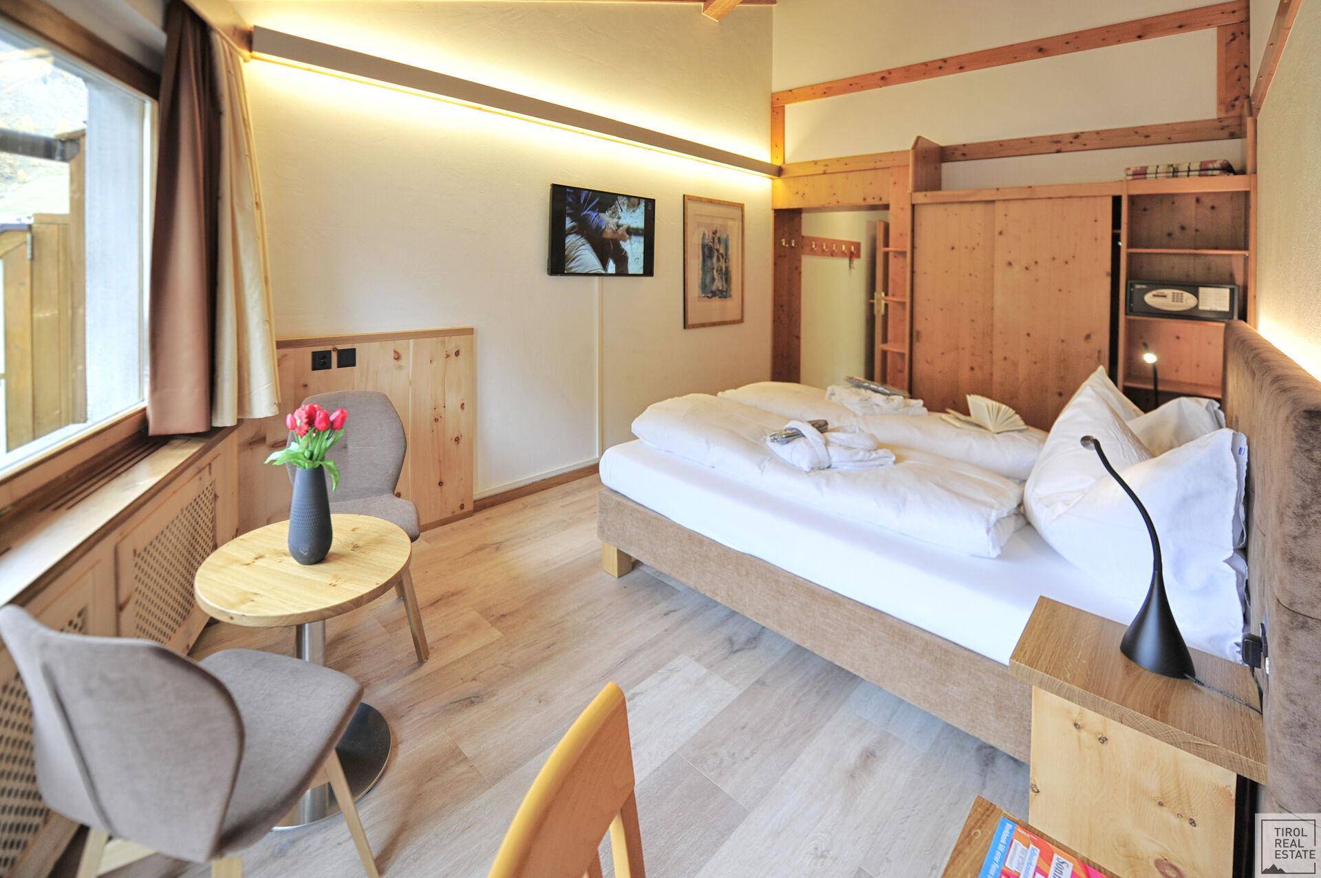 Helles Schlafzimmer mit Holzboden, Fernseher und einem kleinen Tisch mit Stühlen am Fenster.