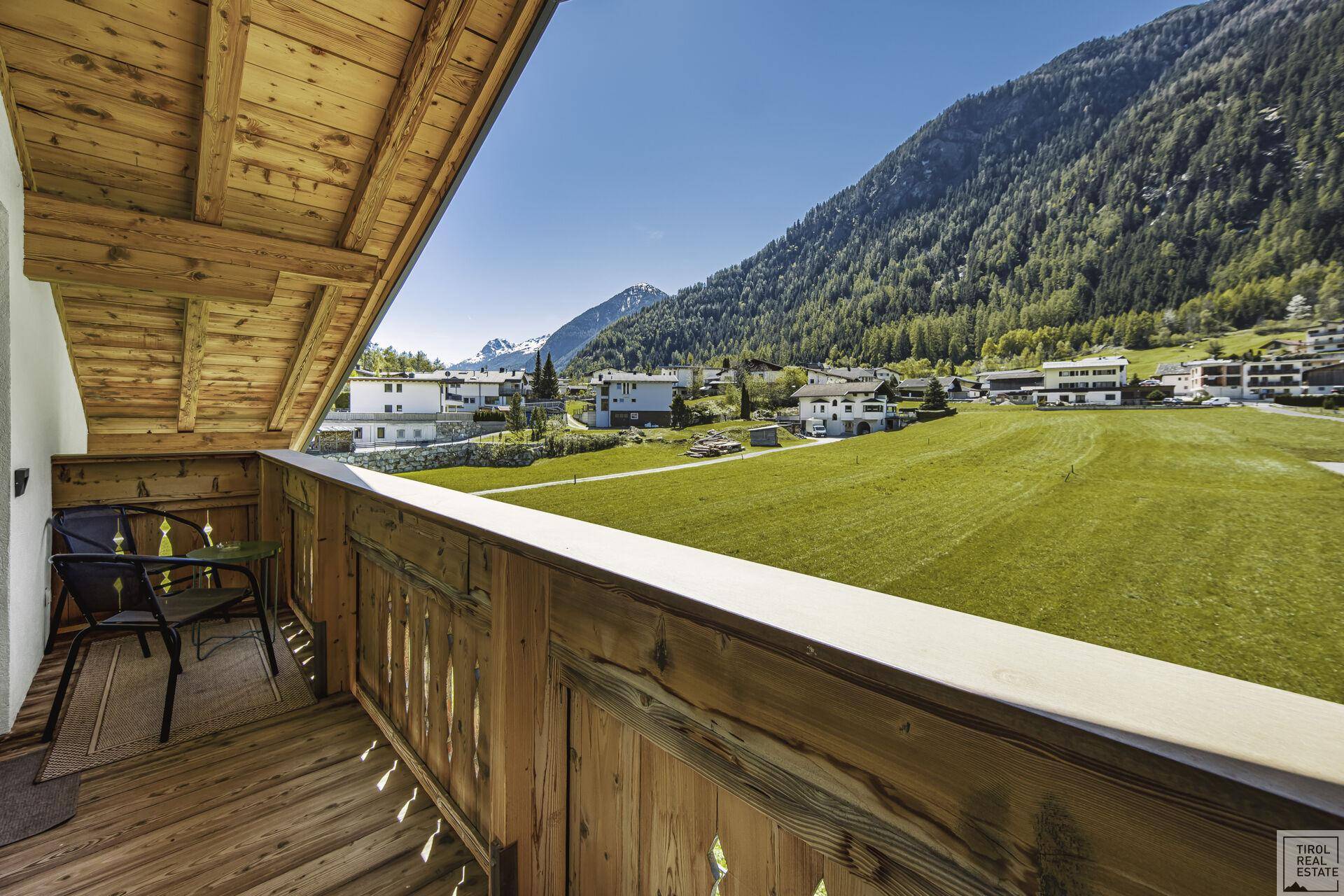 Kleiner Holzbalkon mit Sitzgelegenheiten und weitem Blick auf die grüne Berglandschaft.