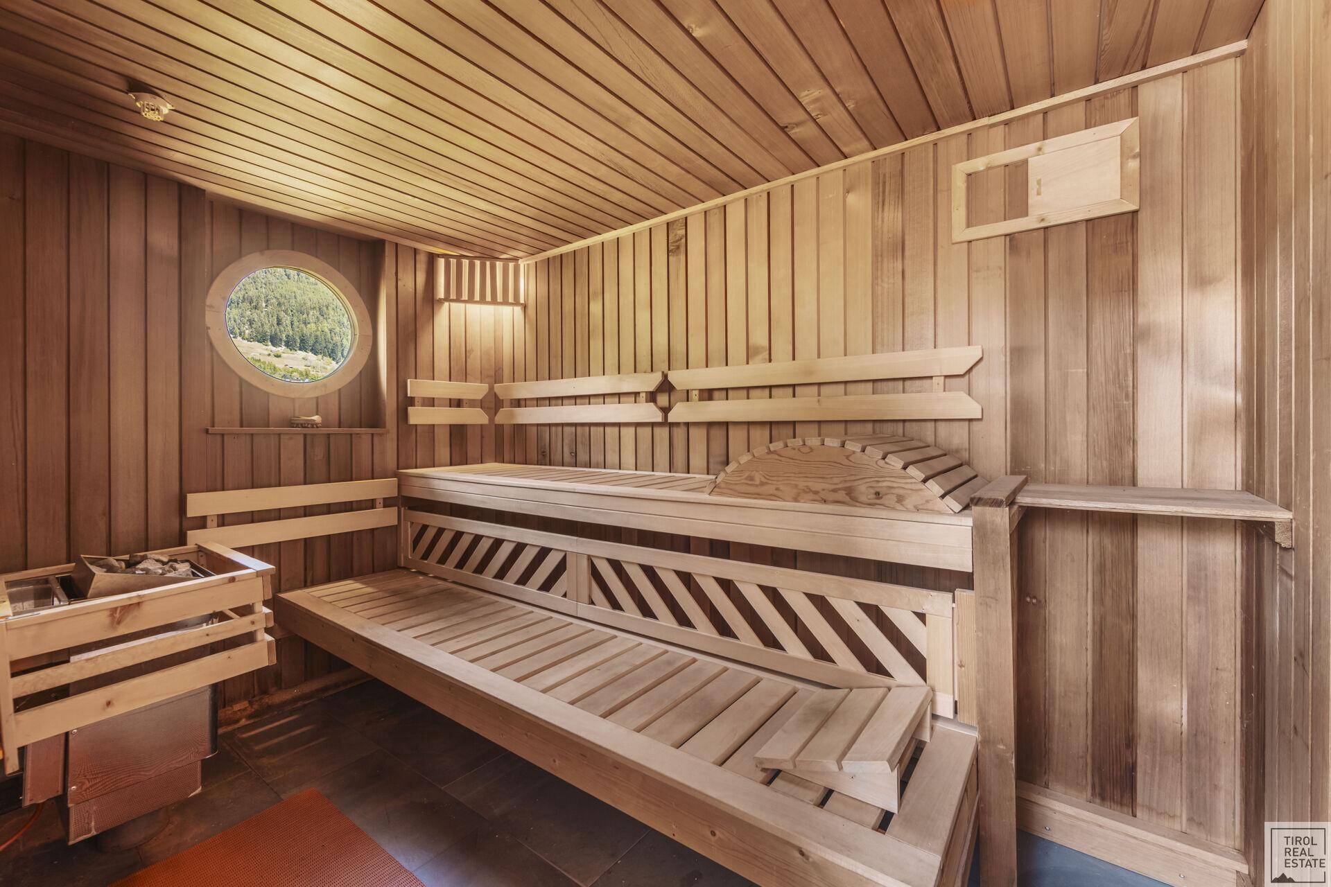 Traditionelle Holzsauna mit bequemen Bänken und einem kleinen runden Fenster.