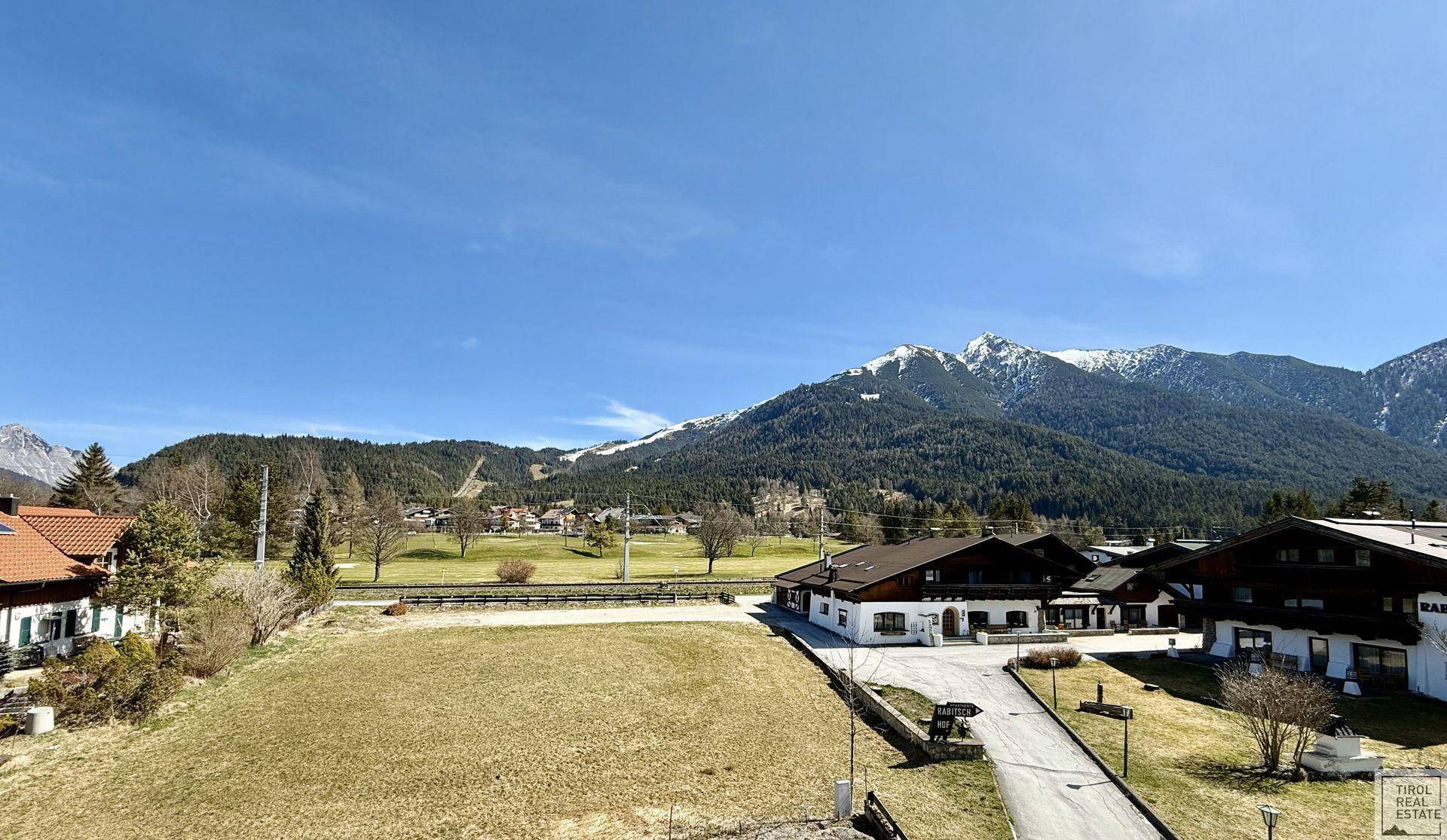 Weitläufiger Blick auf die alpine Landschaft mit schneebedeckten Bergen und grünen Wiesen.