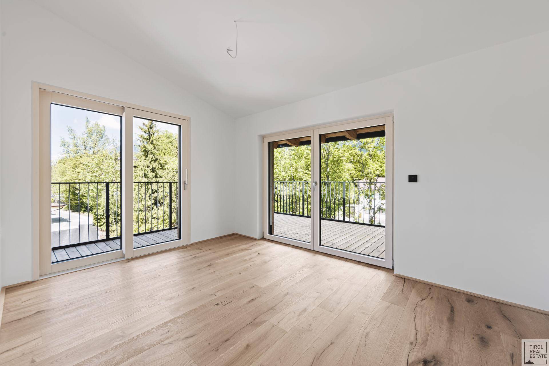 Geräumiges Schlafzimmer mit Parkettboden und zwei großen Schiebetüren zu Balkonen.