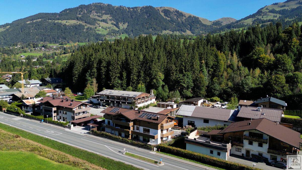Luftaufnahme einer Wohnsiedlung mit traditionellen Häusern und bewaldeten Bergen.