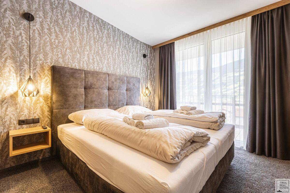 Komfortables Schlafzimmer mit Doppelbett, gemusterter Tapete und Blick auf die Berge.