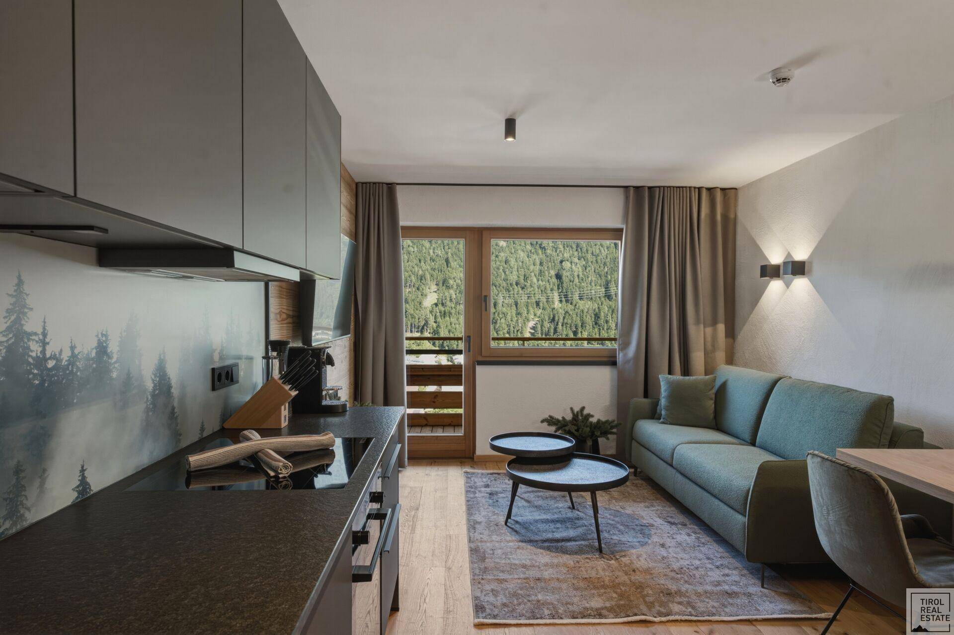 Offener Wohnbereich mit moderner Küchenzeile, Sofa und Blick auf die grüne Landschaft.