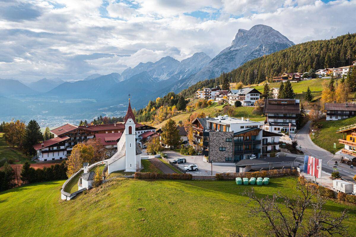 Panoramablick auf ein malerisches Dorf in den Alpen mit Kirche und umliegenden Bergen.