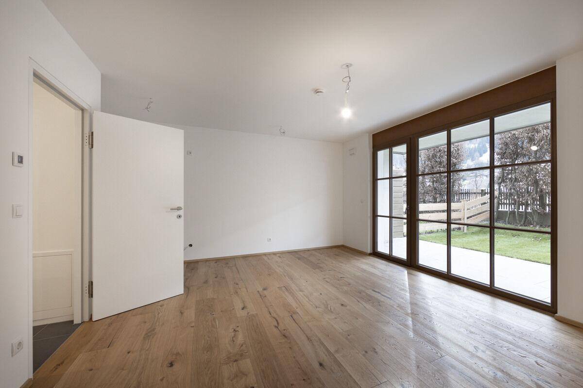 Heller Wohnraum mit großen Fenstern und Zugang zum Garten, ausgestattet mit neuem Holzboden.