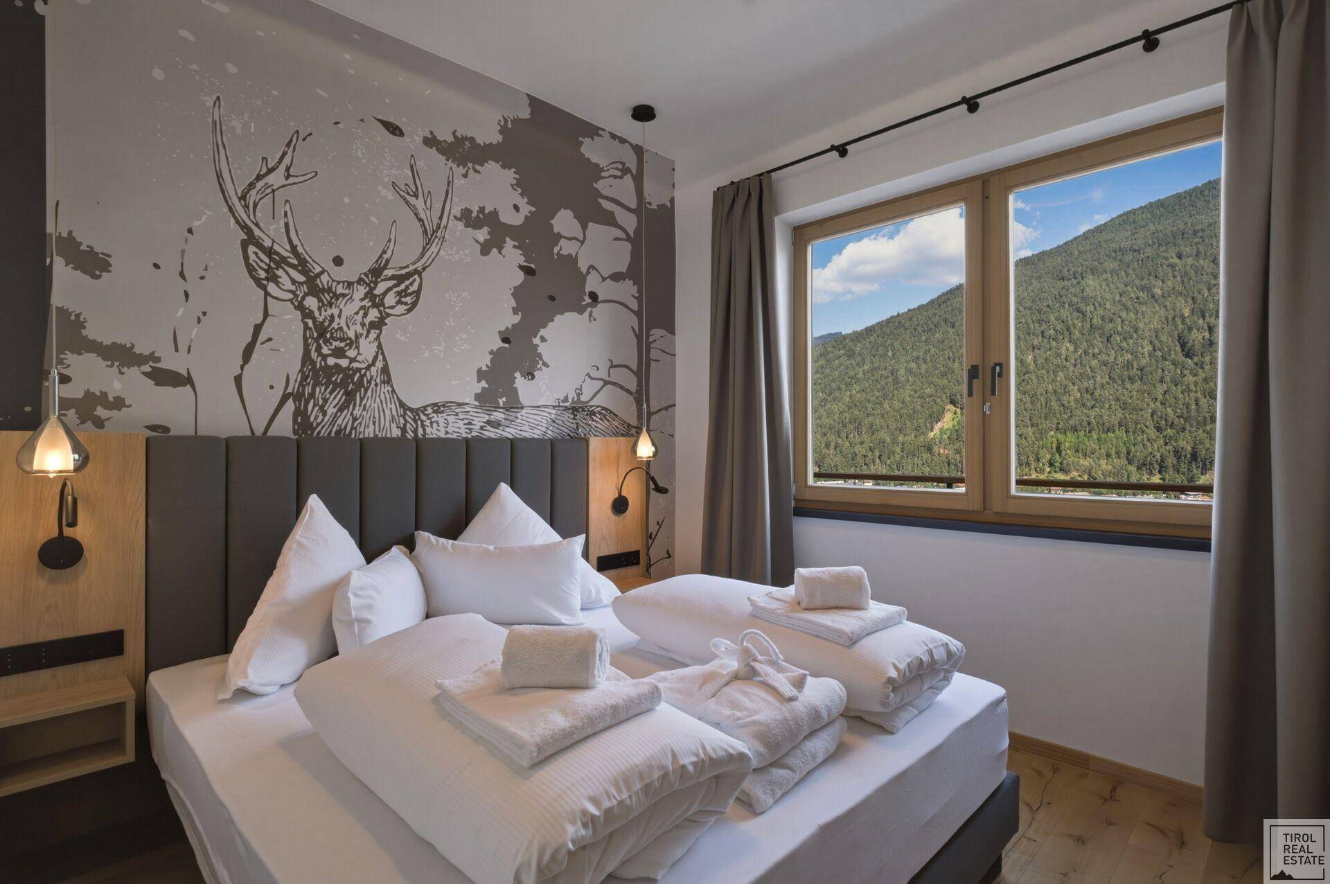 Schlafzimmer mit Doppelbett, Hirschmotiv-Tapete und Bergblick durch das Fenster.
