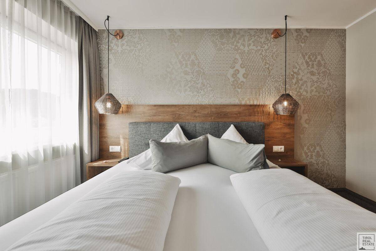 Helles Schlafzimmer mit großem Doppelbett, dekorativer Wandgestaltung und viel Tageslicht durch das Fenster.