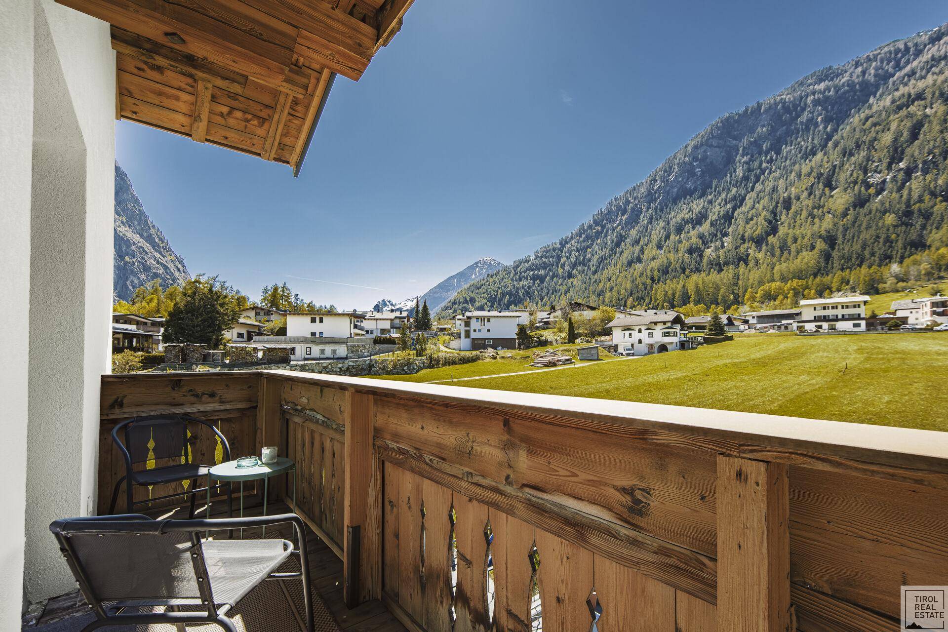 Kleiner Holzbalkon mit Sitzgelegenheiten und weitem Blick auf die grüne Berglandschaft.