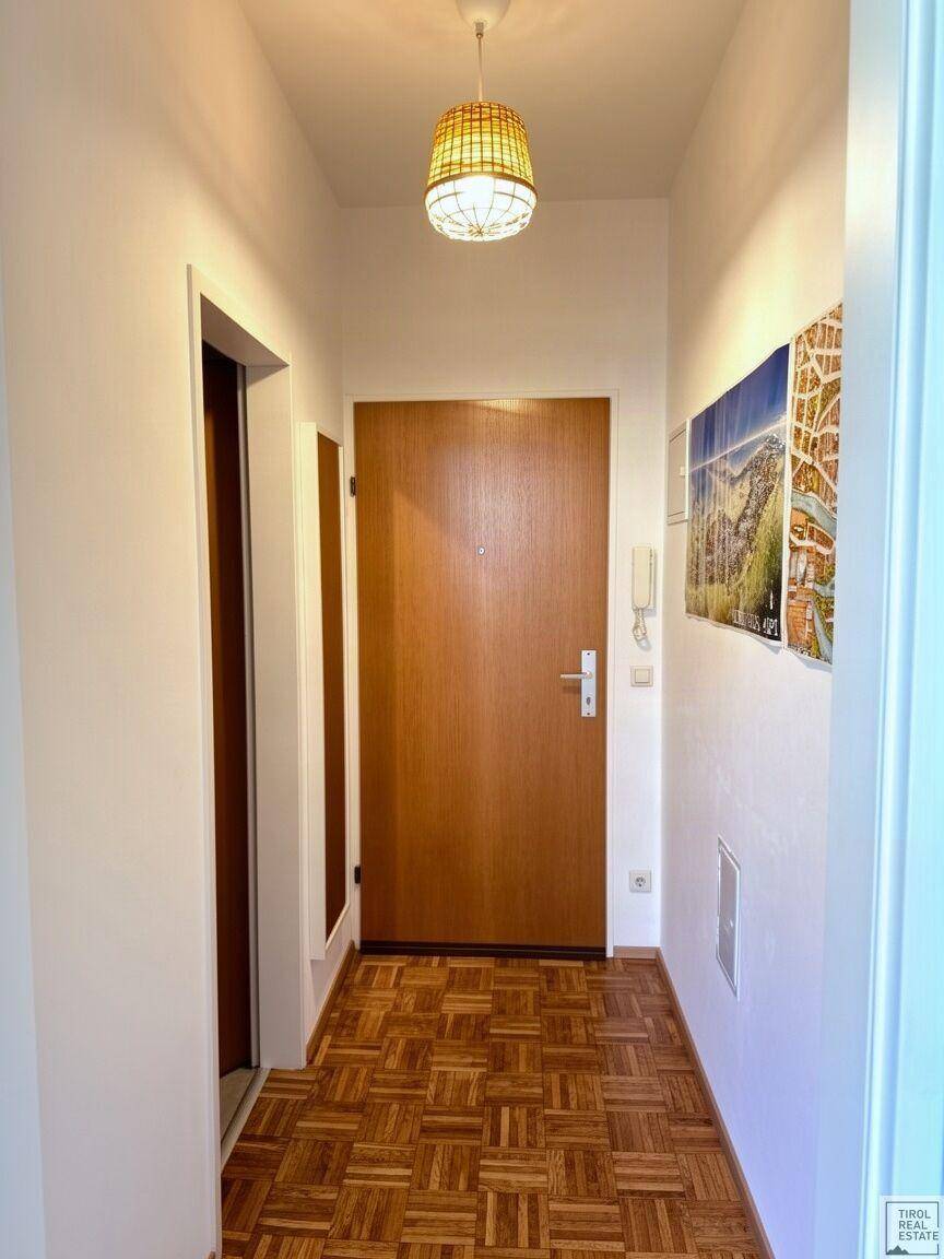 Heller Flur mit Holztür, Parkettboden und einer Deckenleuchte, die den Eingangsbereich erhellt.