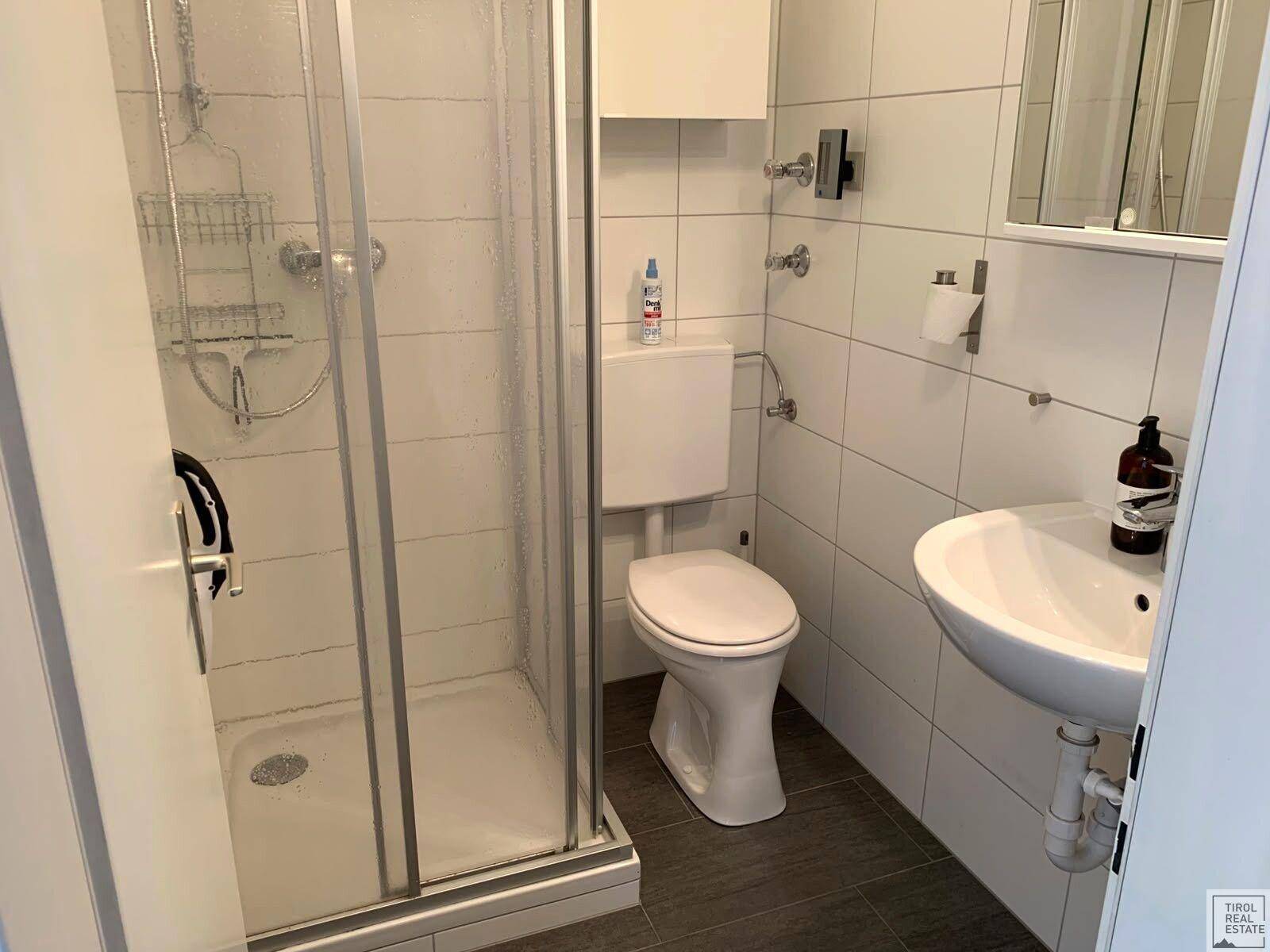 Modernes Badezimmer mit Duschkabine, WC und Waschbecken, ausgestattet mit weißen Fliesen.