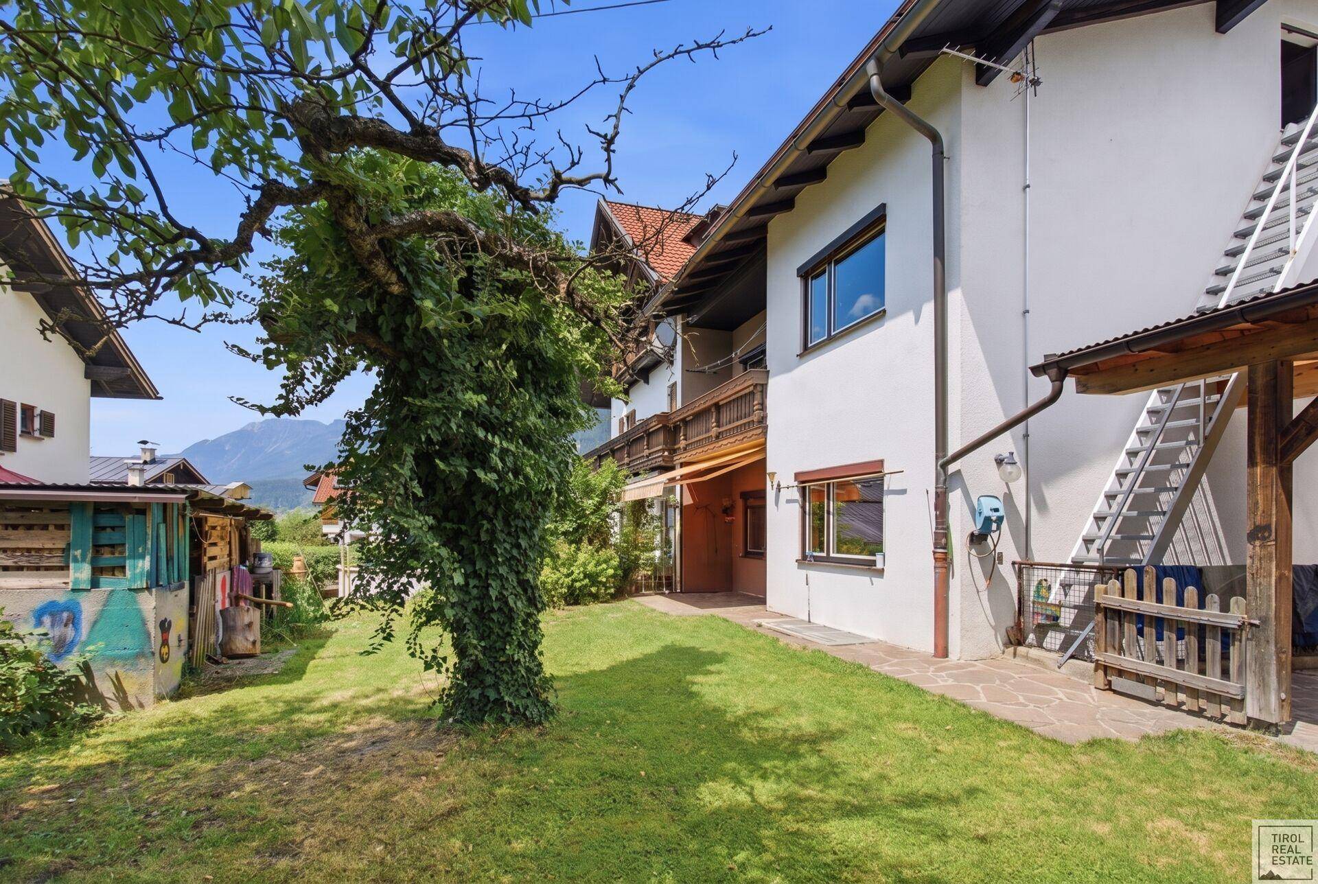 Großer Gartenbereich mit Rasen, Bäumen und Blick auf die Hausfassade.
