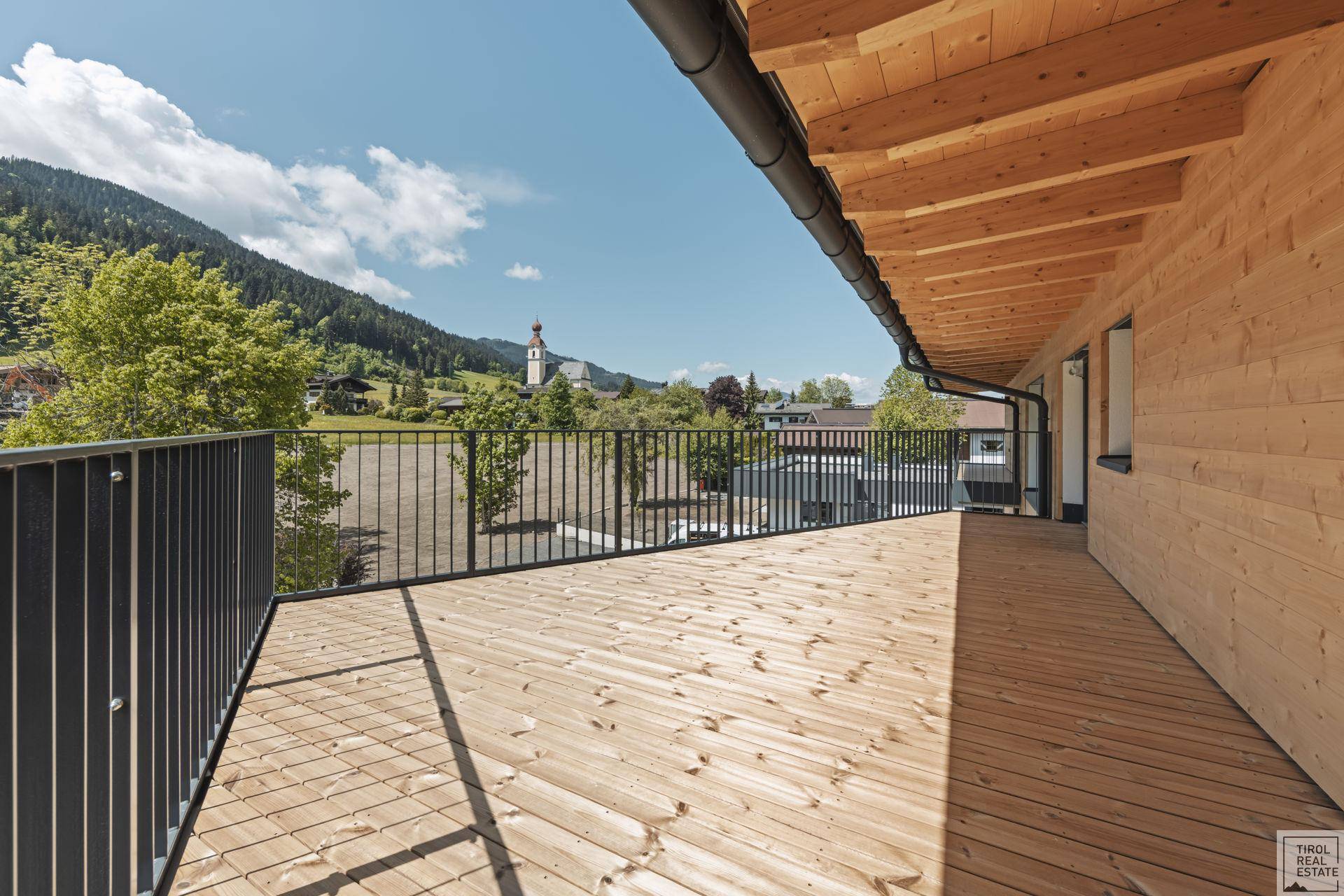Langer Holzbalkon mit Blick auf ein Dorf und die dahinterliegenden Berge.