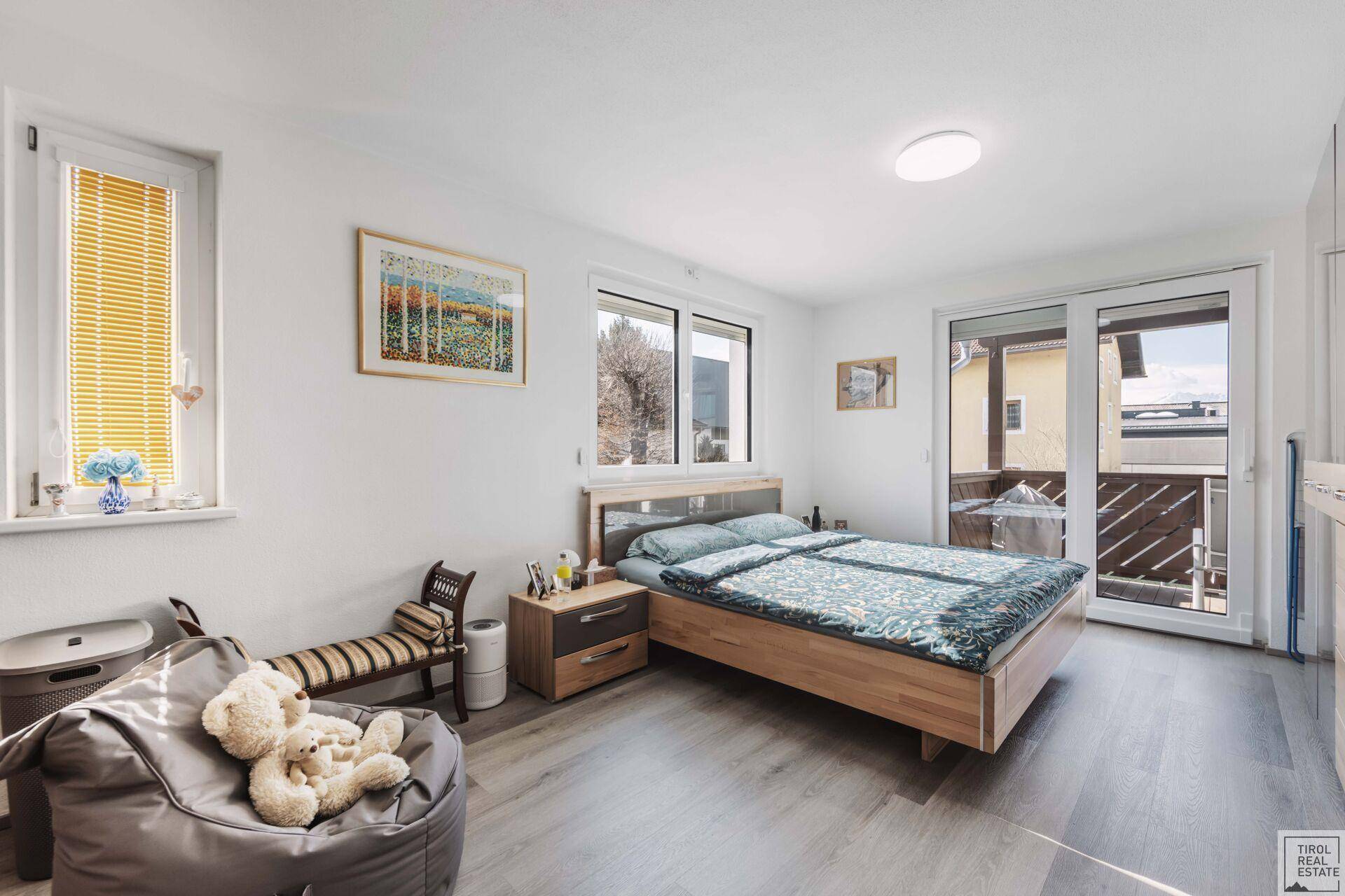 Helles Schlafzimmer mit Doppelbett, Laminatboden und Zugang zum Balkon.