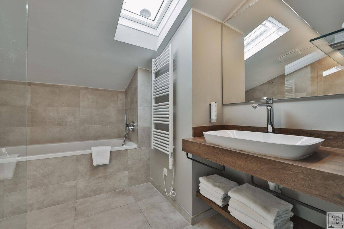 Modernes Badezimmer mit Badewanne, Waschtisch und Dachfenster für natürliches Licht und Belüftung.