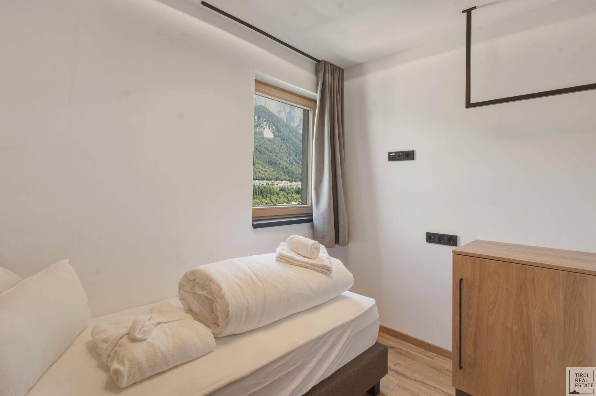 Helles Schlafzimmer mit Einzelbett und Fenster, das einen schönen Bergblick bietet.