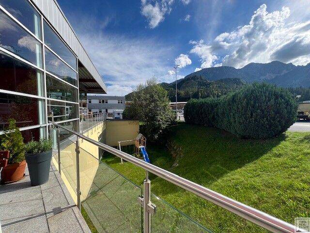 Terrasse mit Glasgeländer und Blick auf einen kleinen Spielplatz sowie die umliegende Naturkulisse.