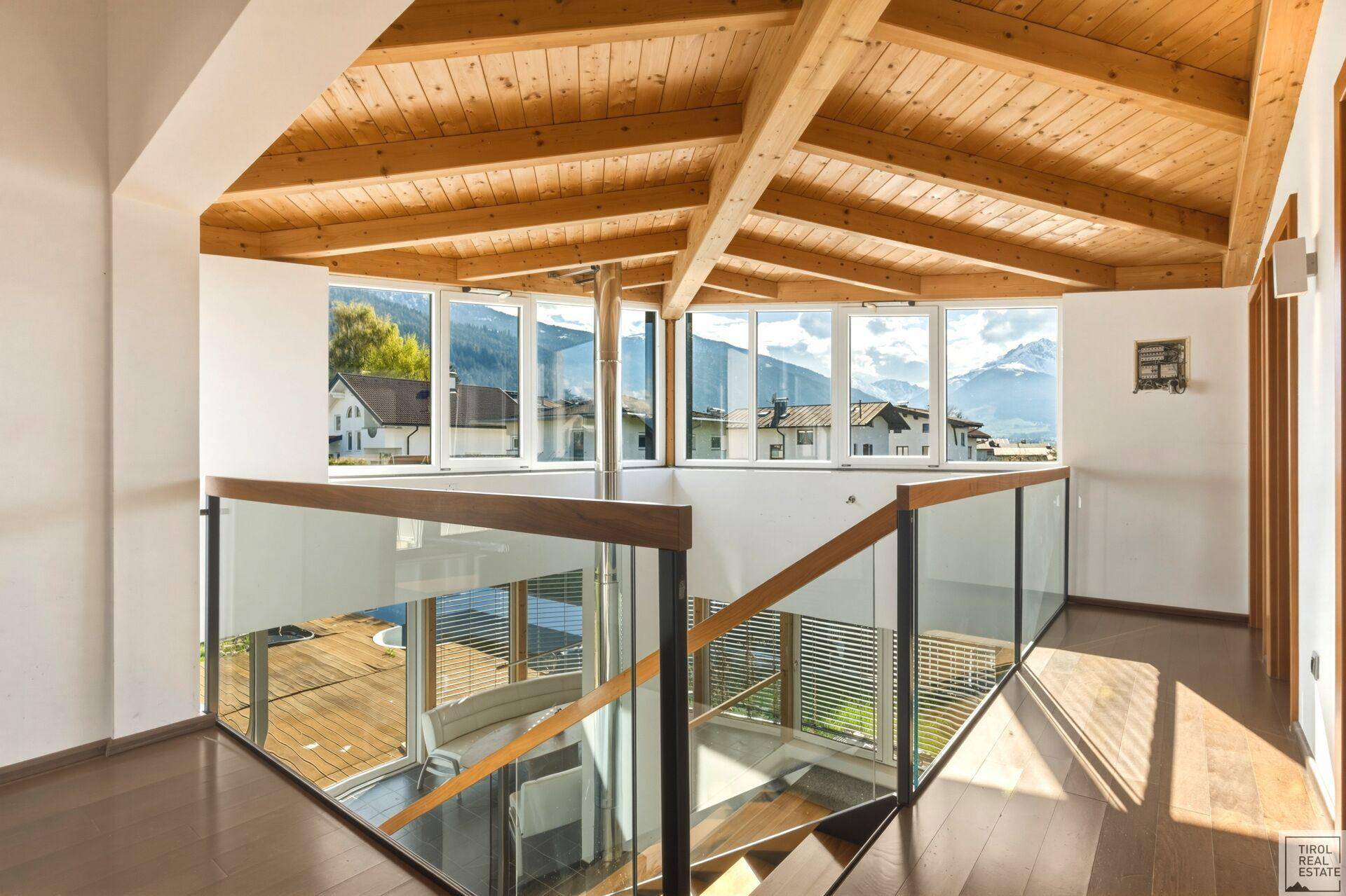Heller Flur im Obergeschoss mit Holzdach, Glasgeländer und Panoramablick auf die Berge.