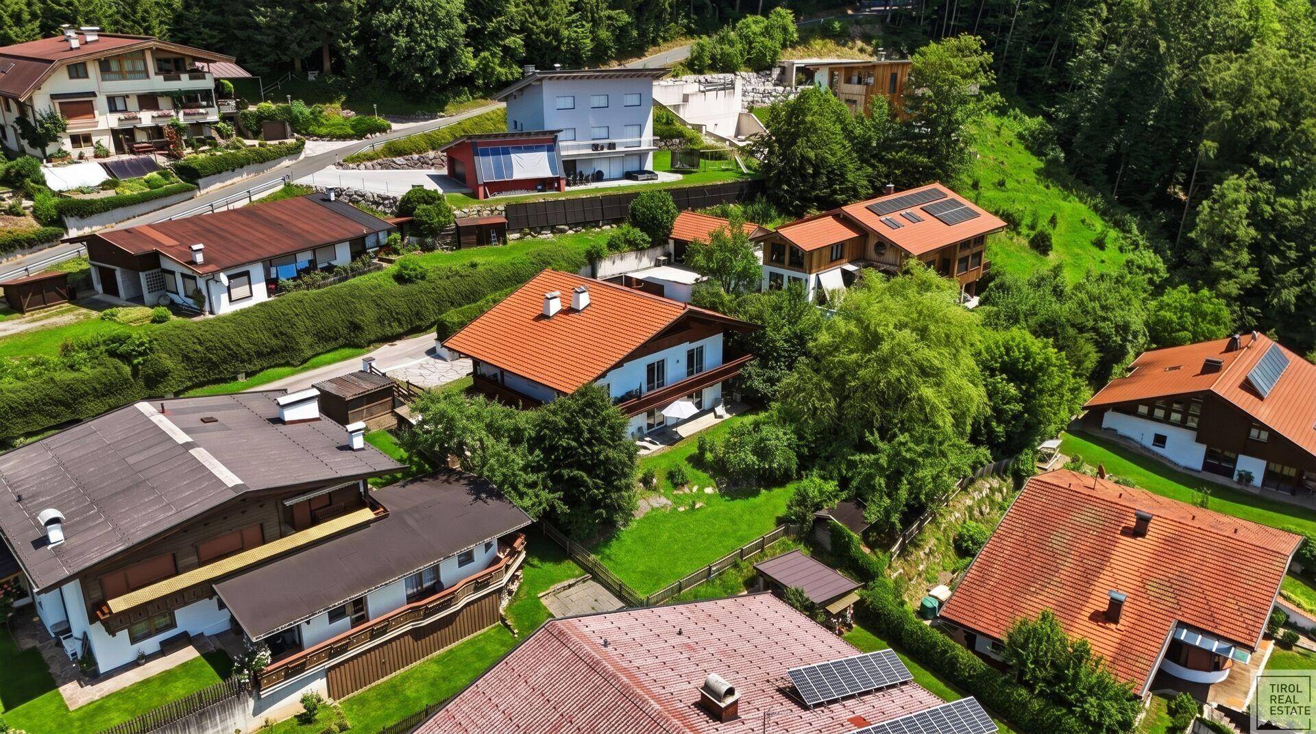 Luftaufnahme eines Hauses mit orangefarbenem Dach, umgeben von viel Grün und anderen Gebäuden in einer Wohnsiedlung.