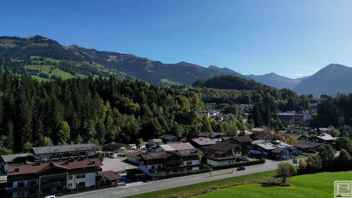 Weitläufige Luftaufnahme einer Wohnsiedlung eingebettet in eine grüne Landschaft mit majestätischen Bergen im Hintergrund.