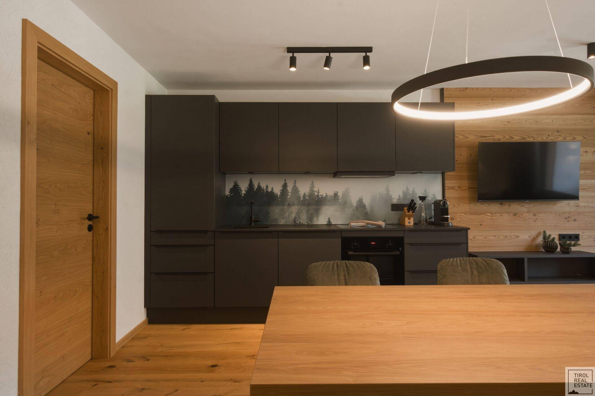 Moderne Küche mit dunklen Schränken und Holztisch, integriert in einen offenen Wohnbereich.