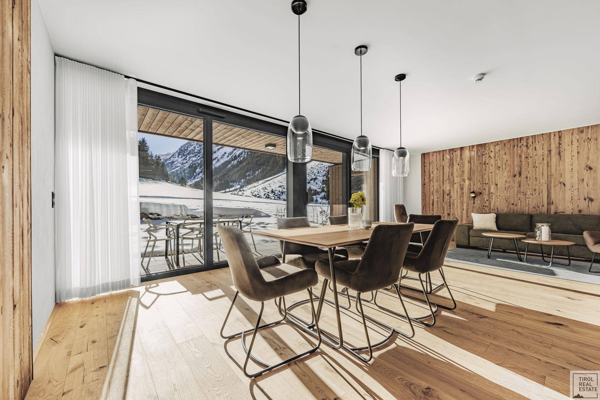 Heller Essbereich mit Holztisch und Blick auf die verschneite Berglandschaft, angrenzend an den Wohnbereich.