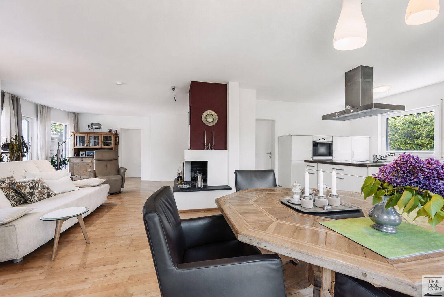Offener Wohn- und Essbereich mit Kamin, Holzboden und Blick auf die moderne Küche.