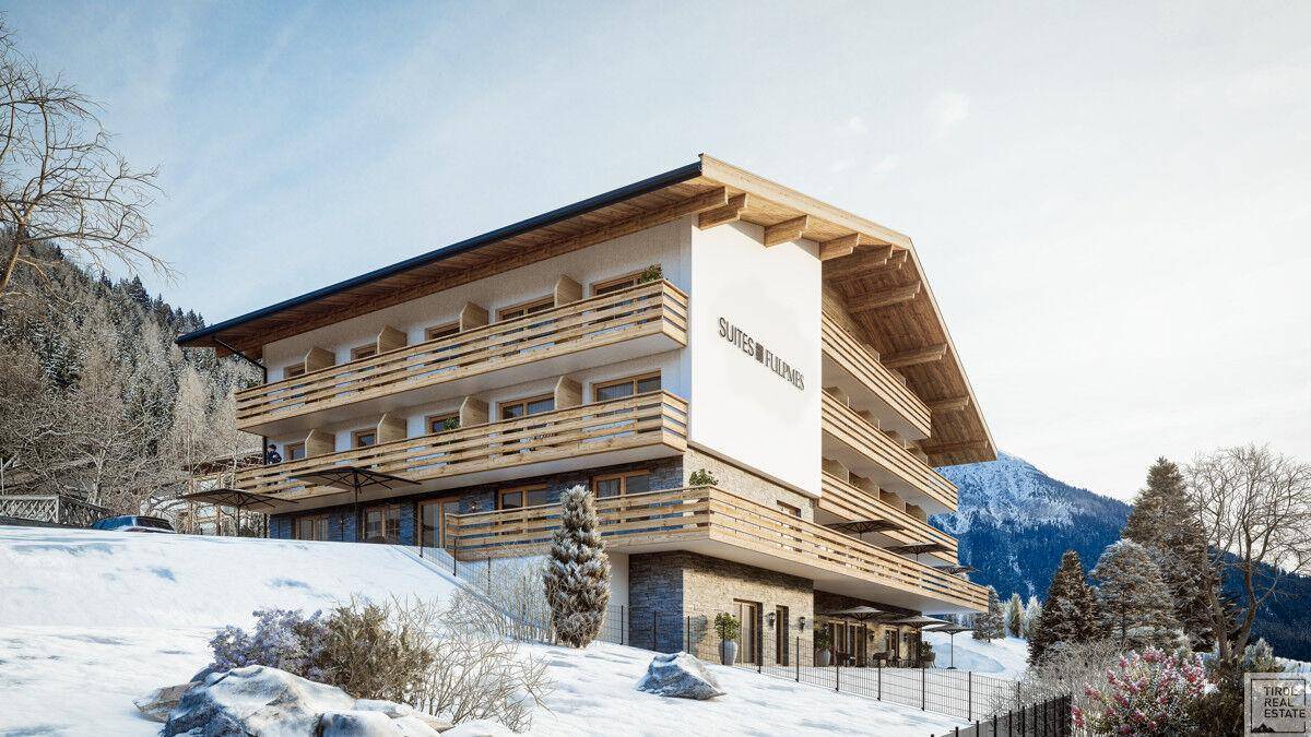 Modernes Gebäude im alpinen Stil mit Holzfassade und Balkonen, eingebettet in verschneite Natur.