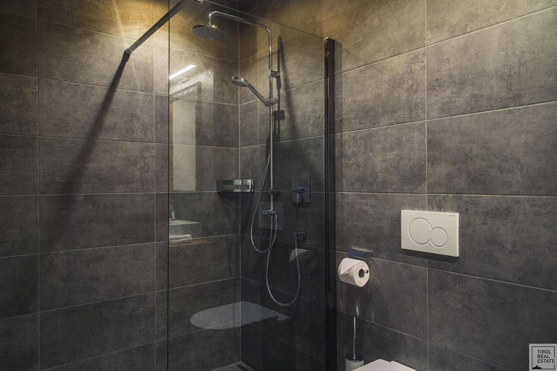 Modernes Badezimmer mit großer begehbarer Dusche und dunklen Fliesen.